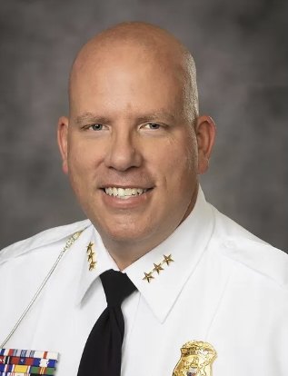 Bald man in white police chief dress uniform with gold stars, badge, and service ribbons.