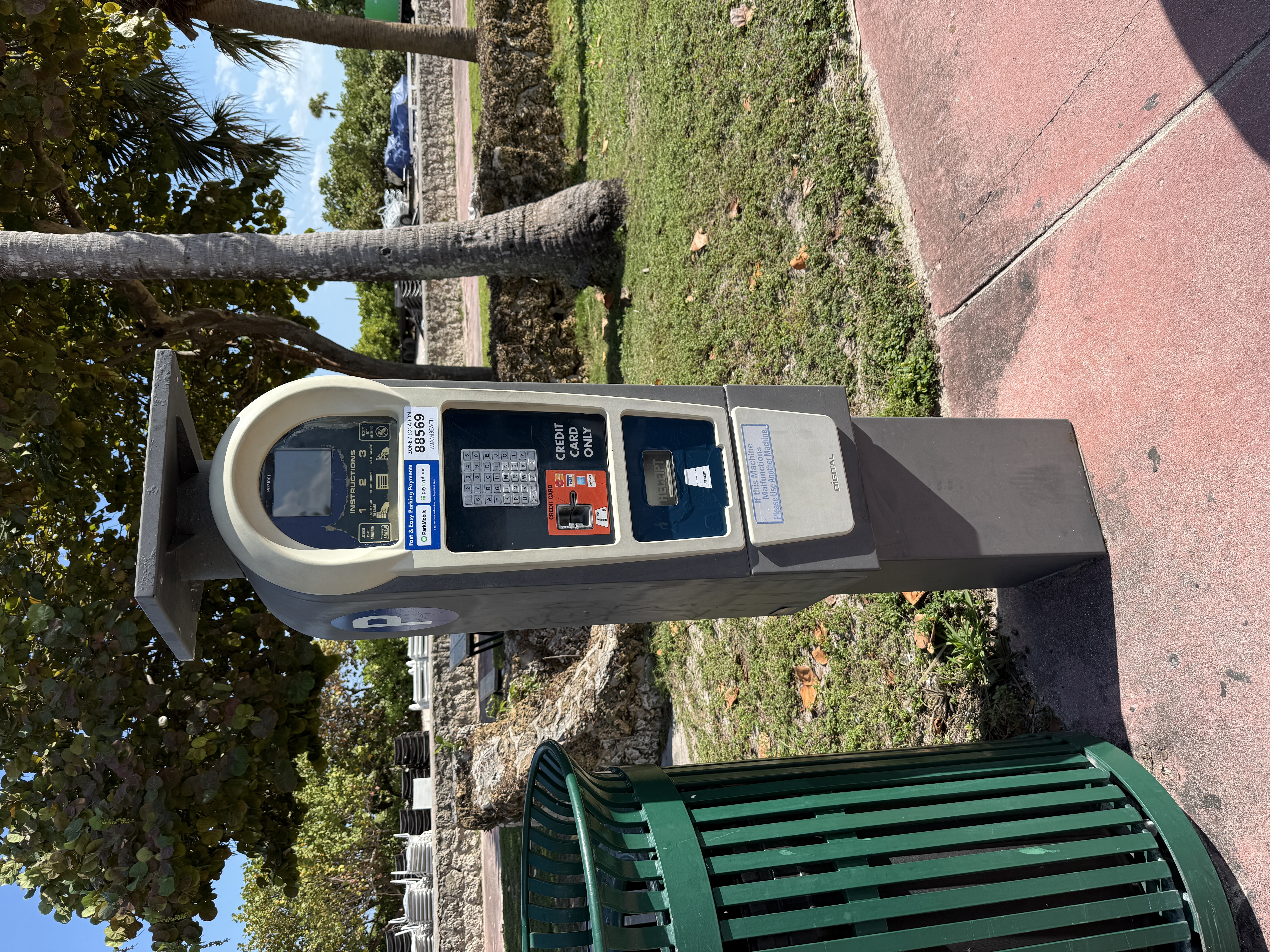 Solar-powered parking pay station on a sidewalk near palm trees.