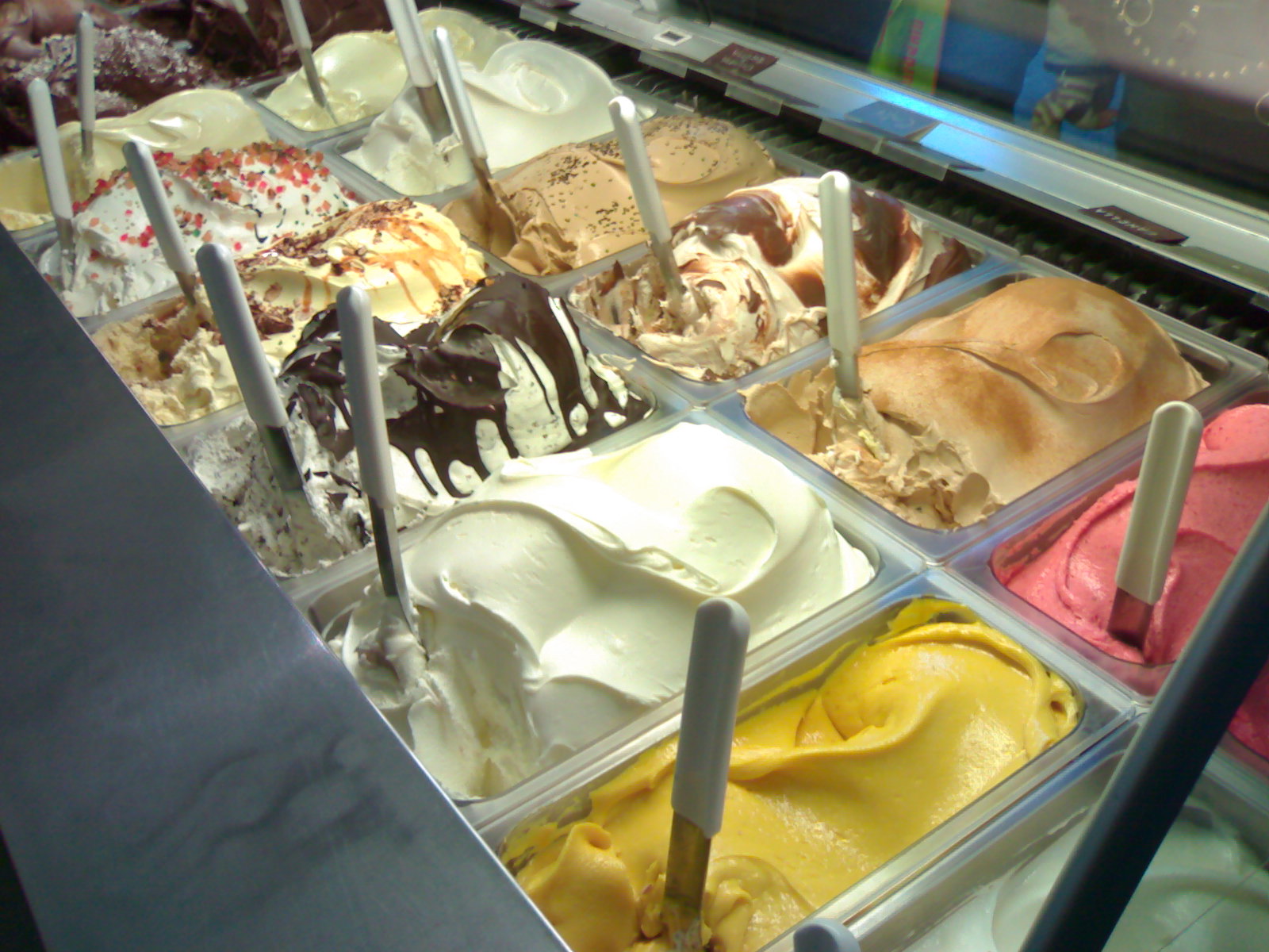 A gelato display case holds rows of flavors in metal pans.