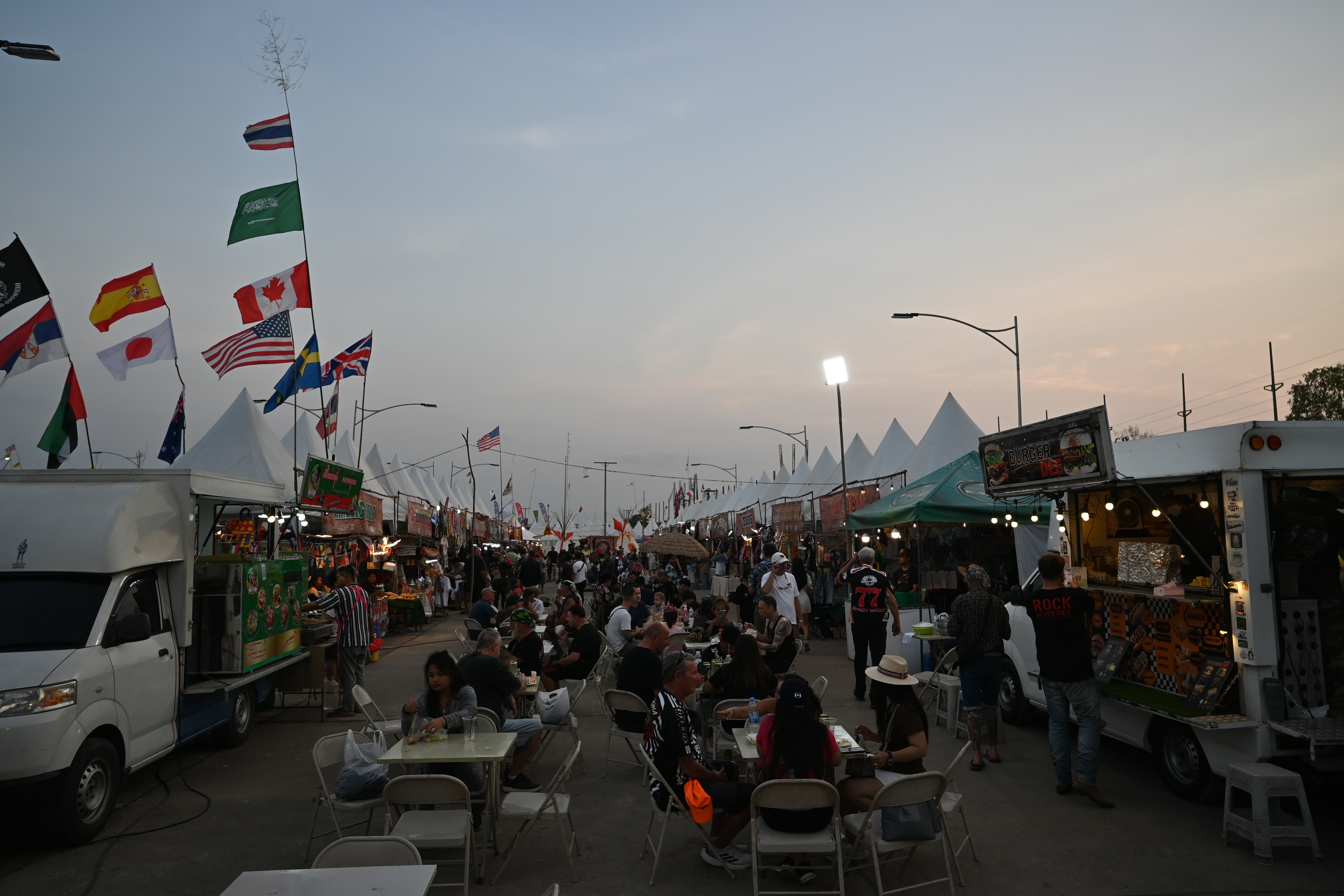 Rows of food trucks and vendor stalls along a busy outdoor walkway at dusk.
