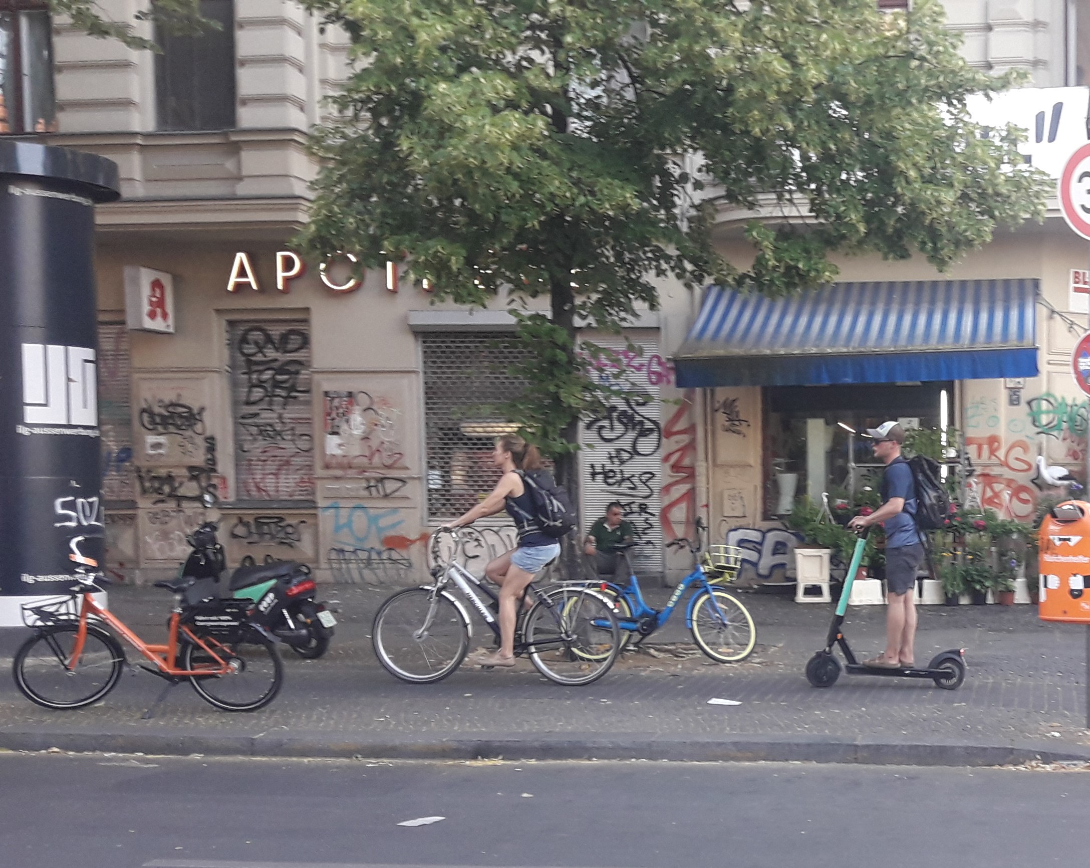 A person rides an electric scooter on a sidewalk next to parked bicycles in a city.