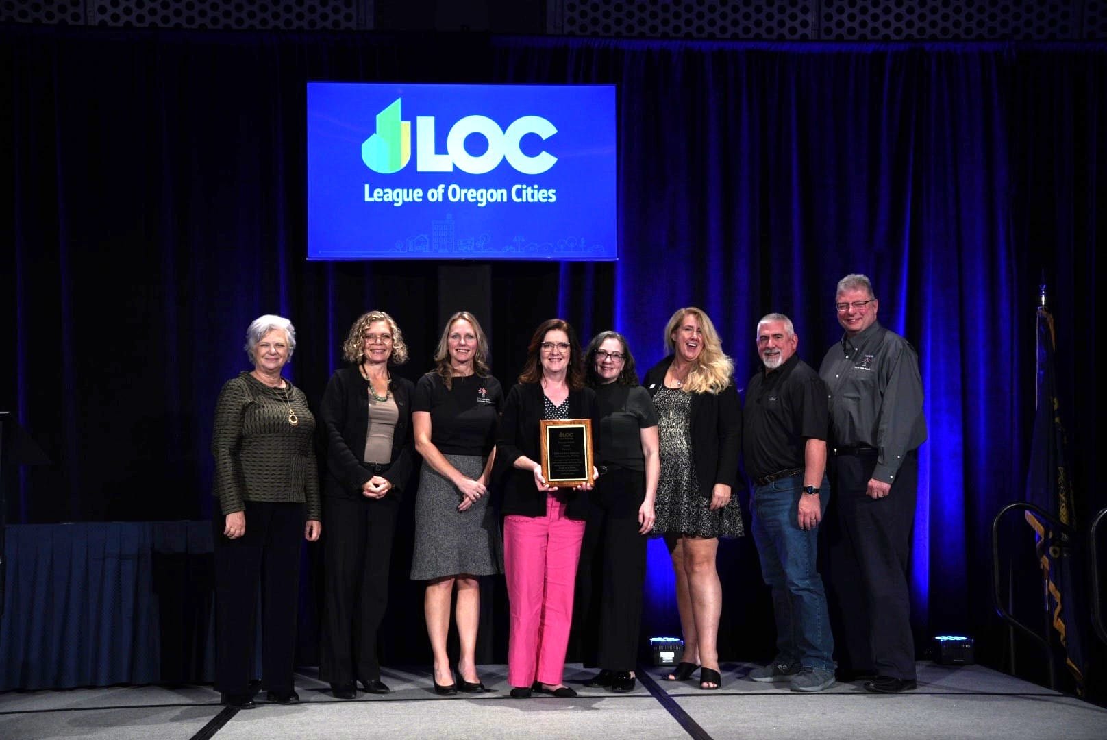 Group of eight people posing in front of a League of Oregon Cities backdrop at an awards ceremony.