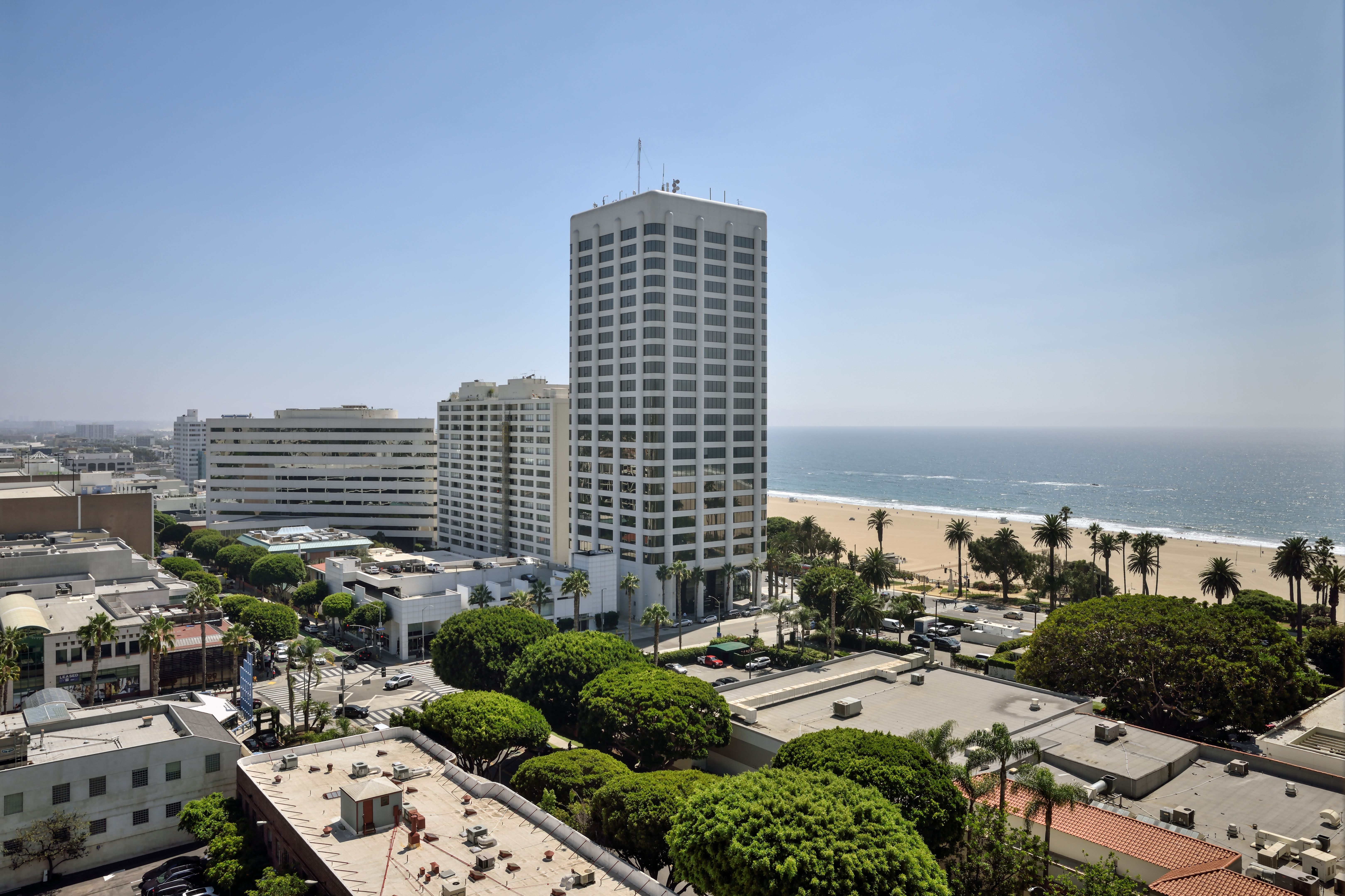 Aerial view of downtown Santa Monica with palm trees, buildings, beach, and ocean.