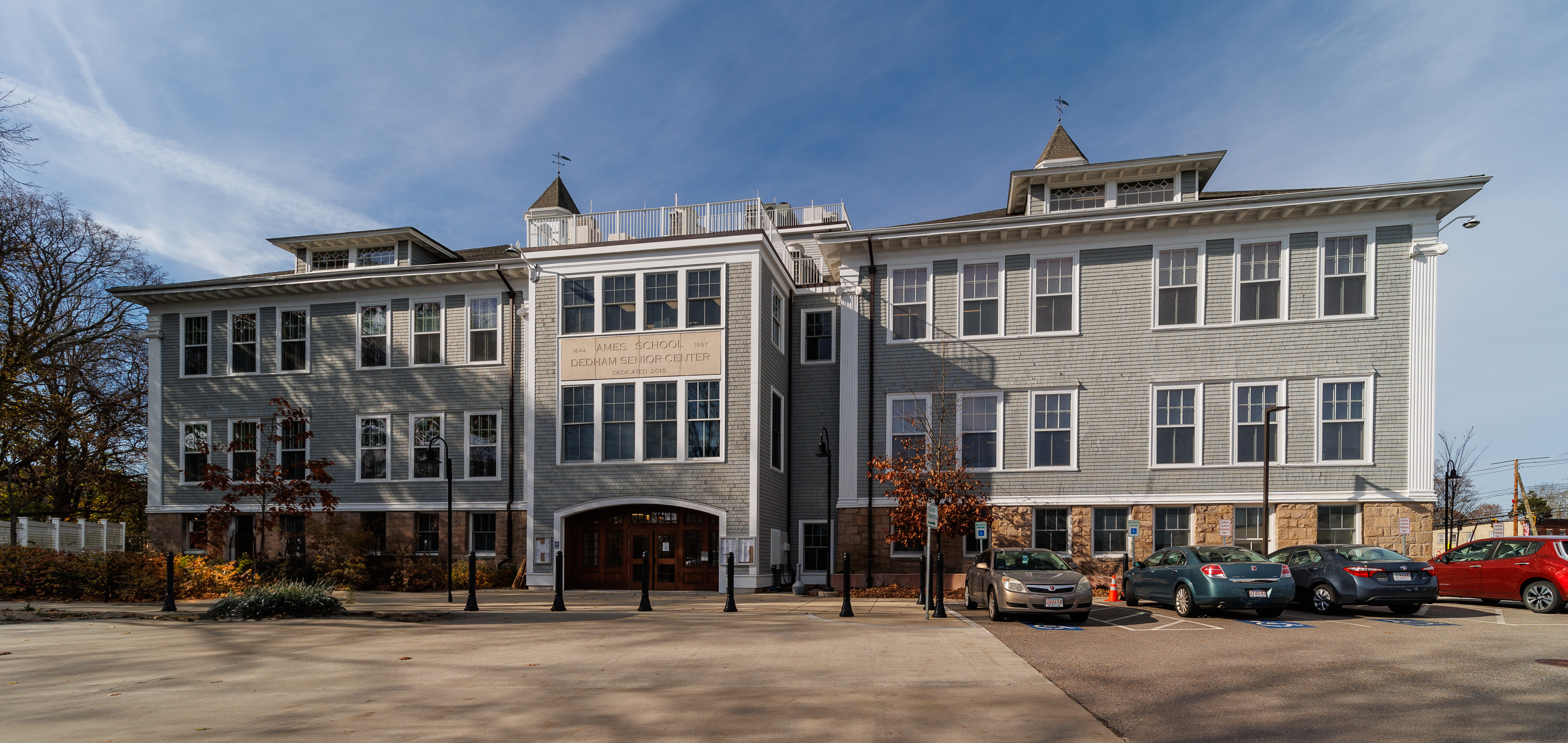 Rear view of a large gray institutional building with a parking lot in the foreground.