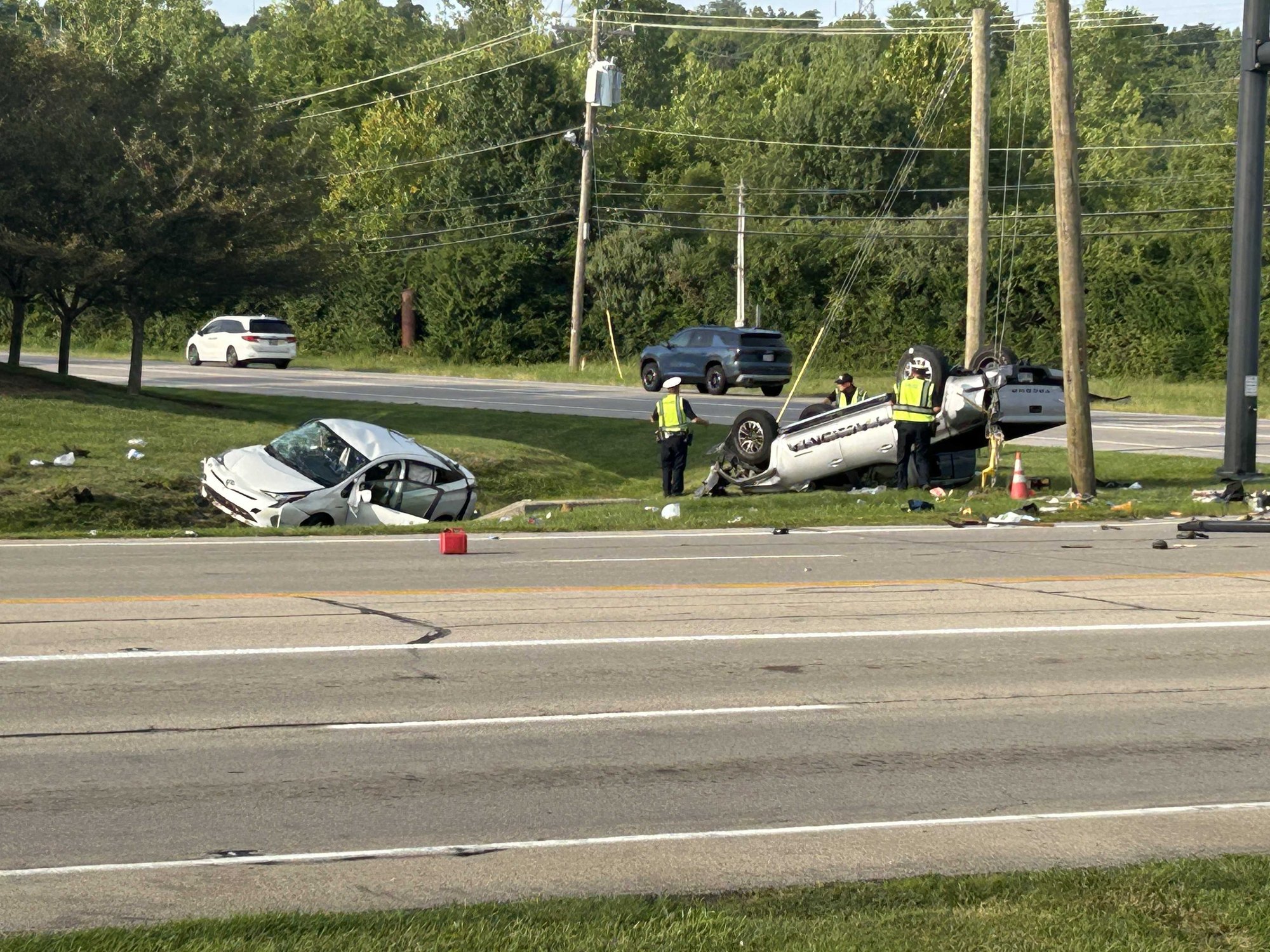 Overturned vehicle on grass median with emergency responders in high-visibility vests nearby.