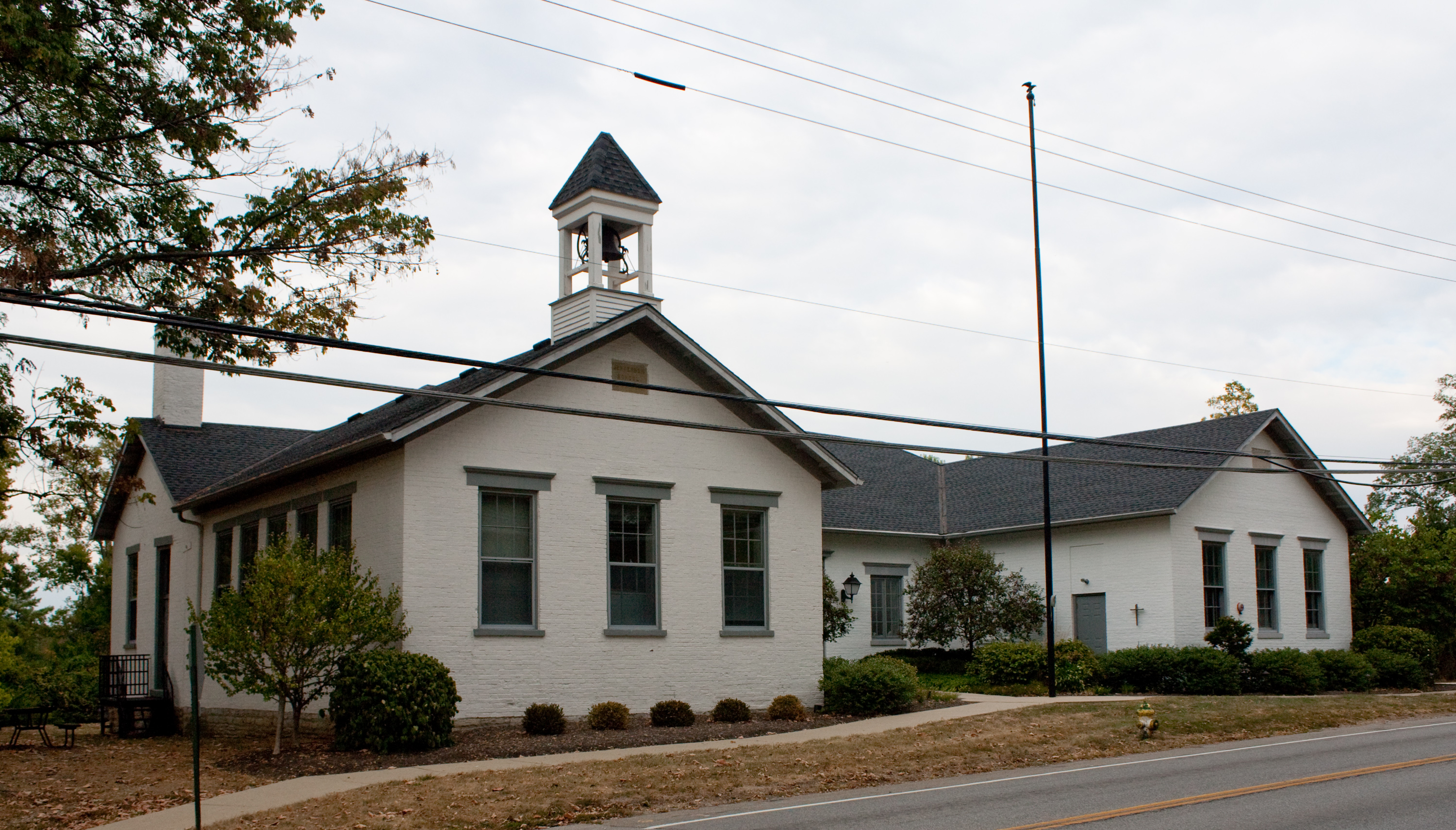 White brick schoolhouse with a bell tower cupola surrounded by trees.