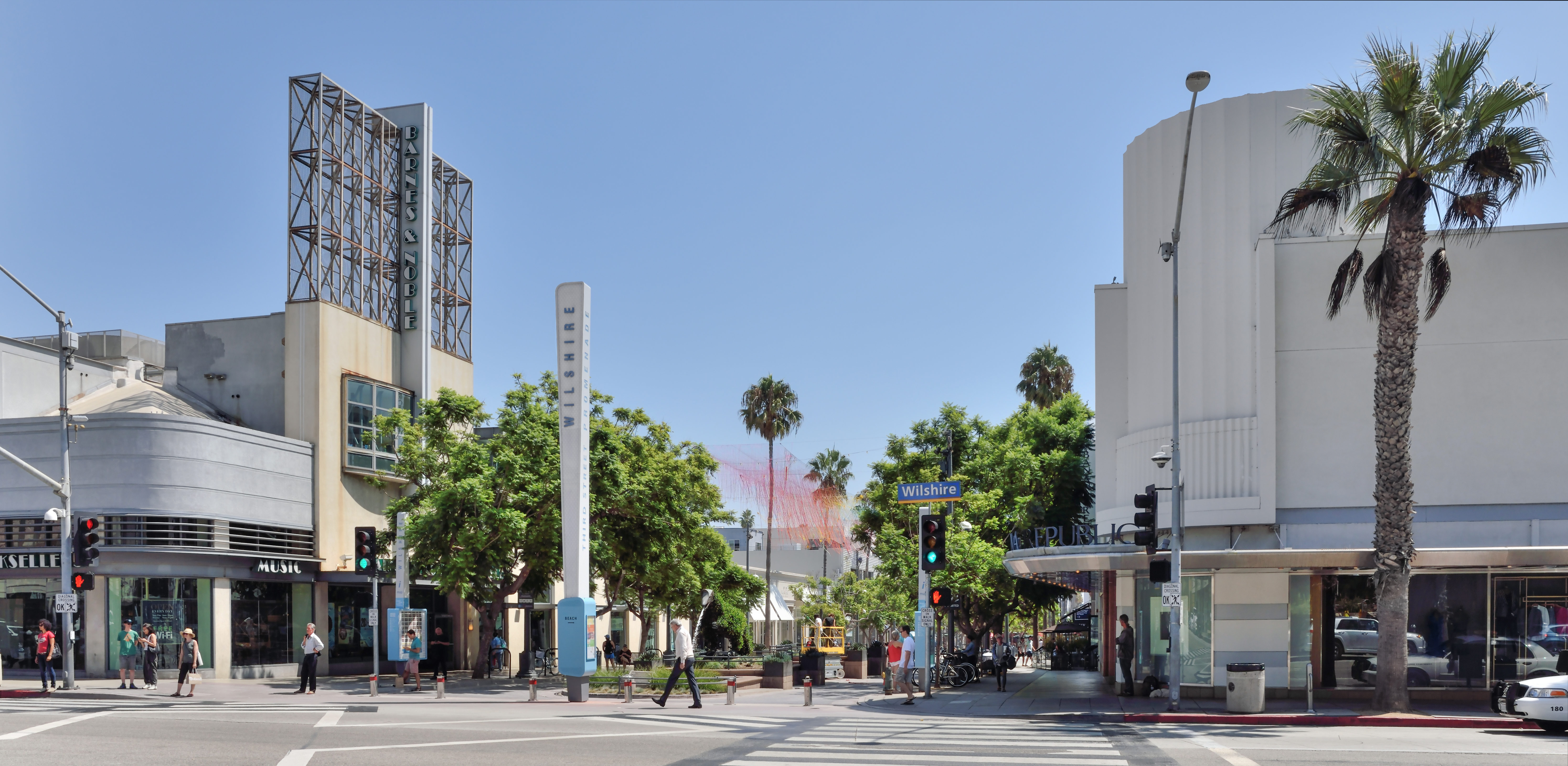 Pedestrian promenade lined with palm trees and storefronts stretching south from a busy intersection.