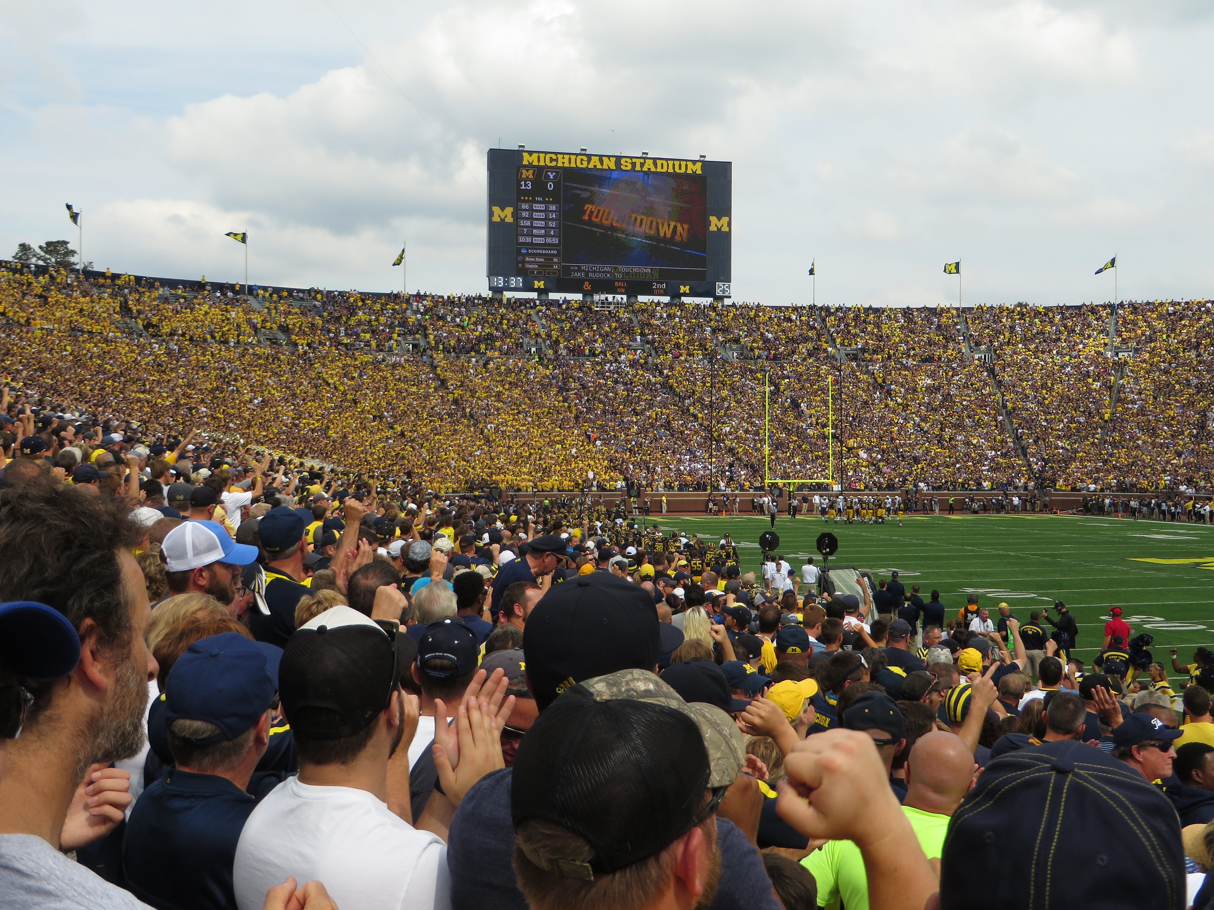 Michigan Stadium scoreboard reading TOUCHDOWN and MICHIGAN STADIUM with a packed crowd below.