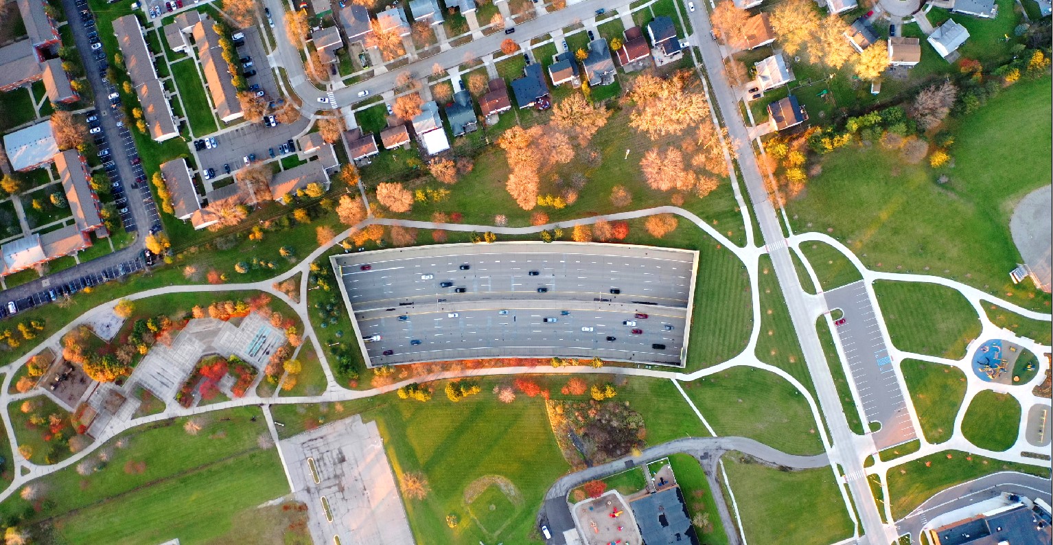 Aerial view of a multi-lane freeway with green pedestrian plazas and suburban neighborhoods on both sides.