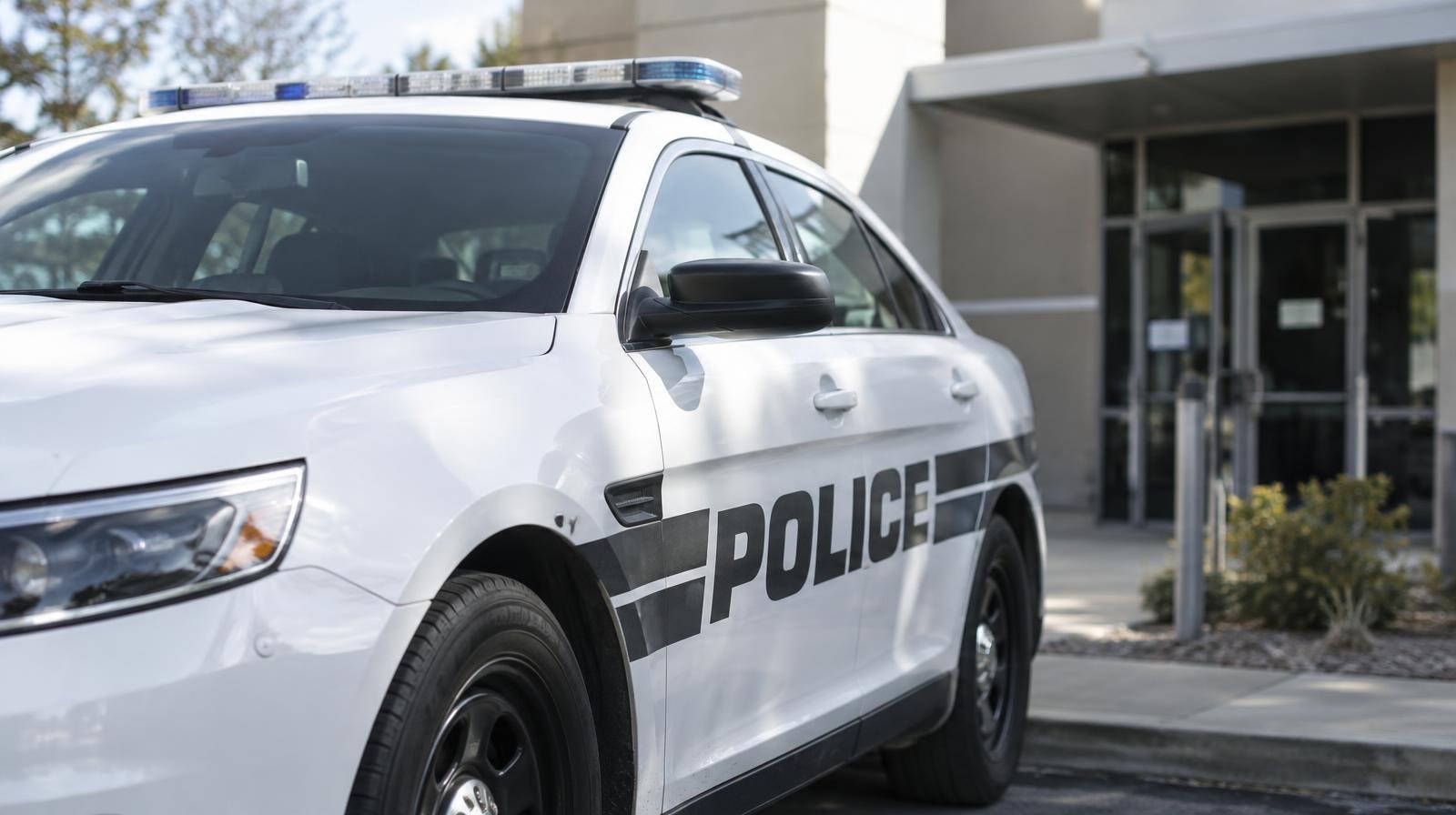 White police patrol car parked outside a plain office building under a clear sky.