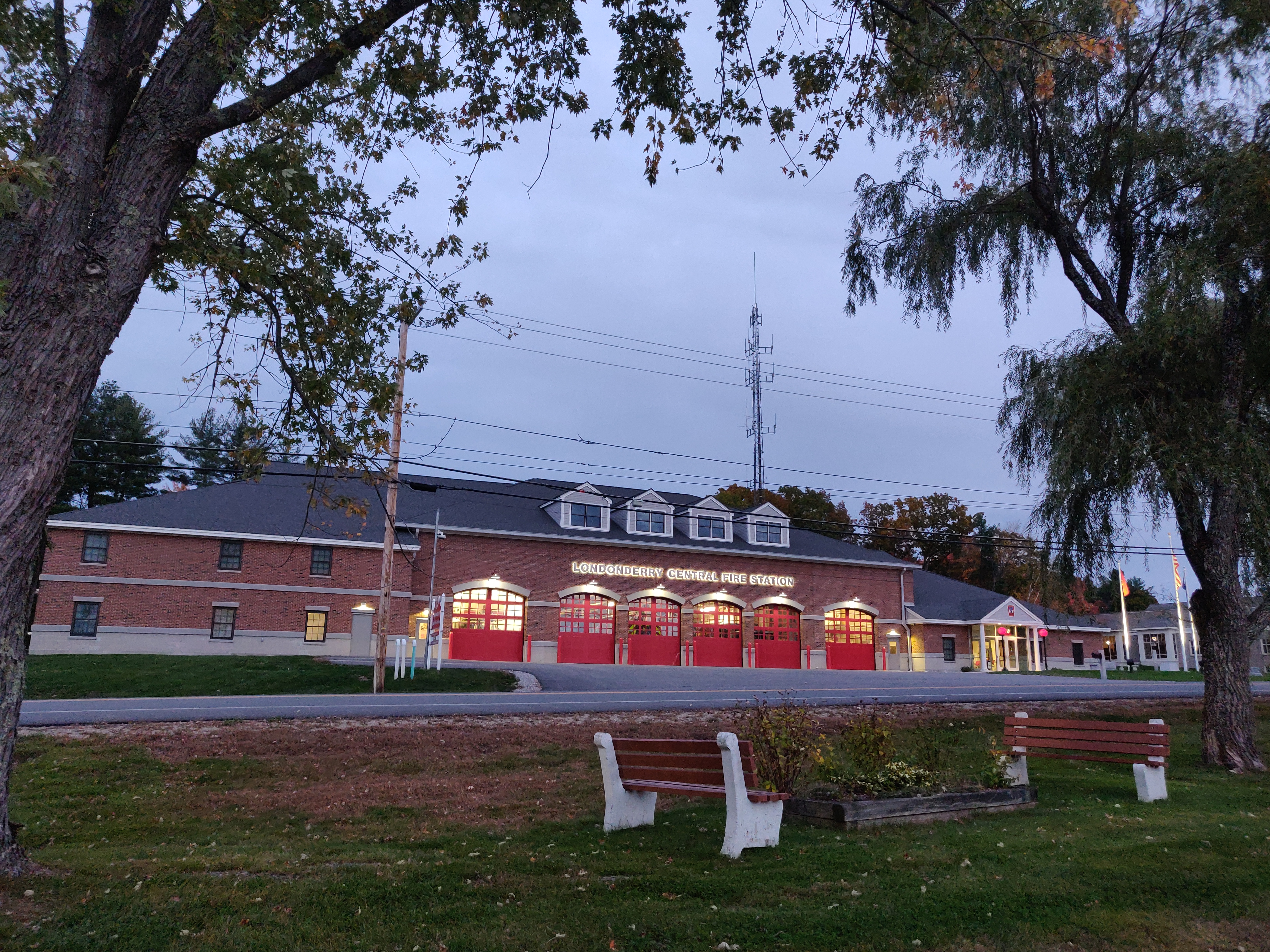 Brick fire station building with red garage doors and a communications tower at dusk.