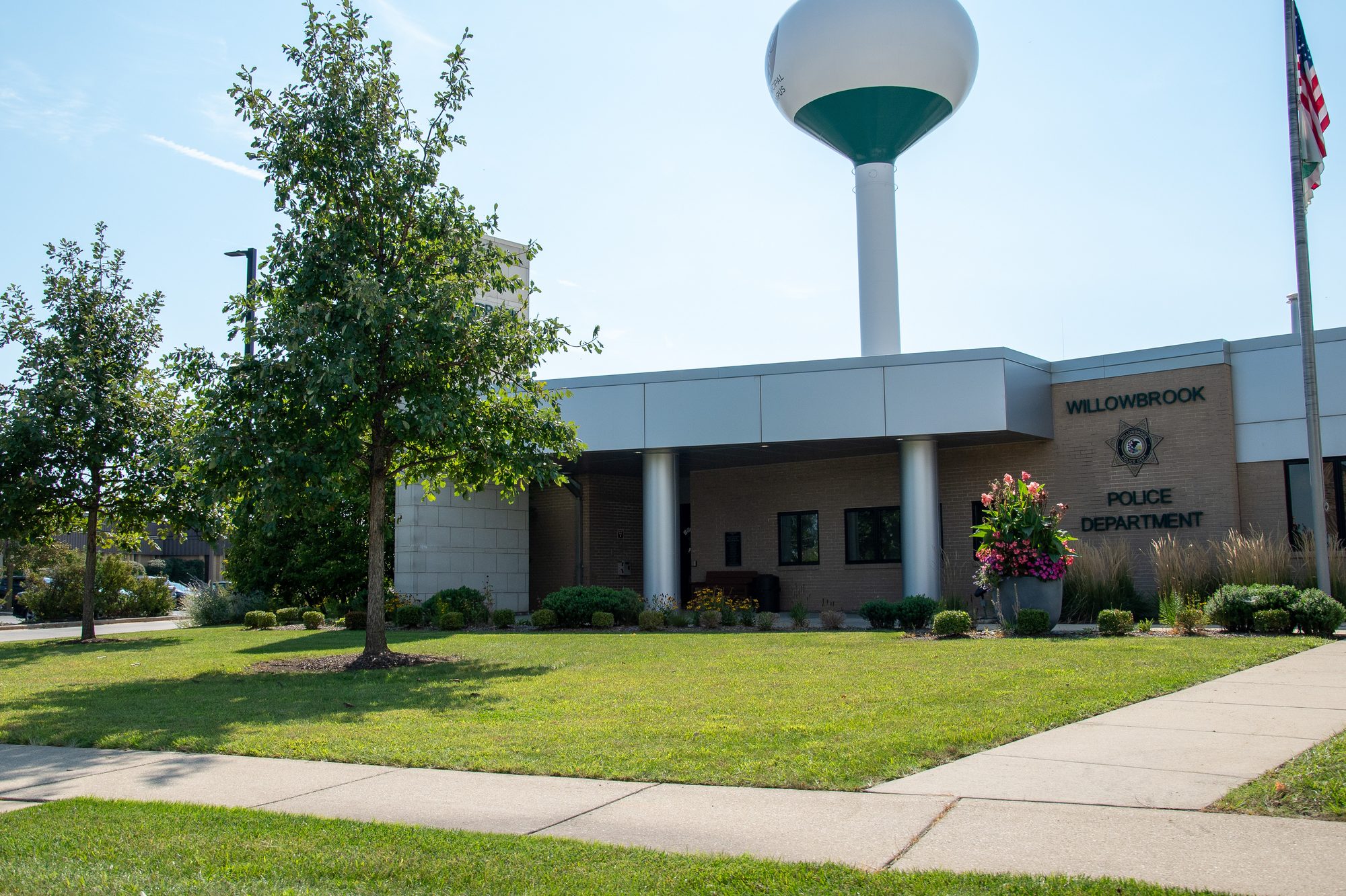 Exterior of a tan brick police department building with white columns and an American flag.