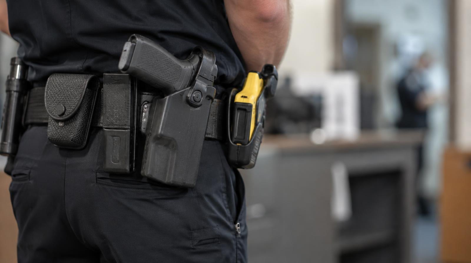 Close-up of a police duty belt with a holstered pistol and taser.