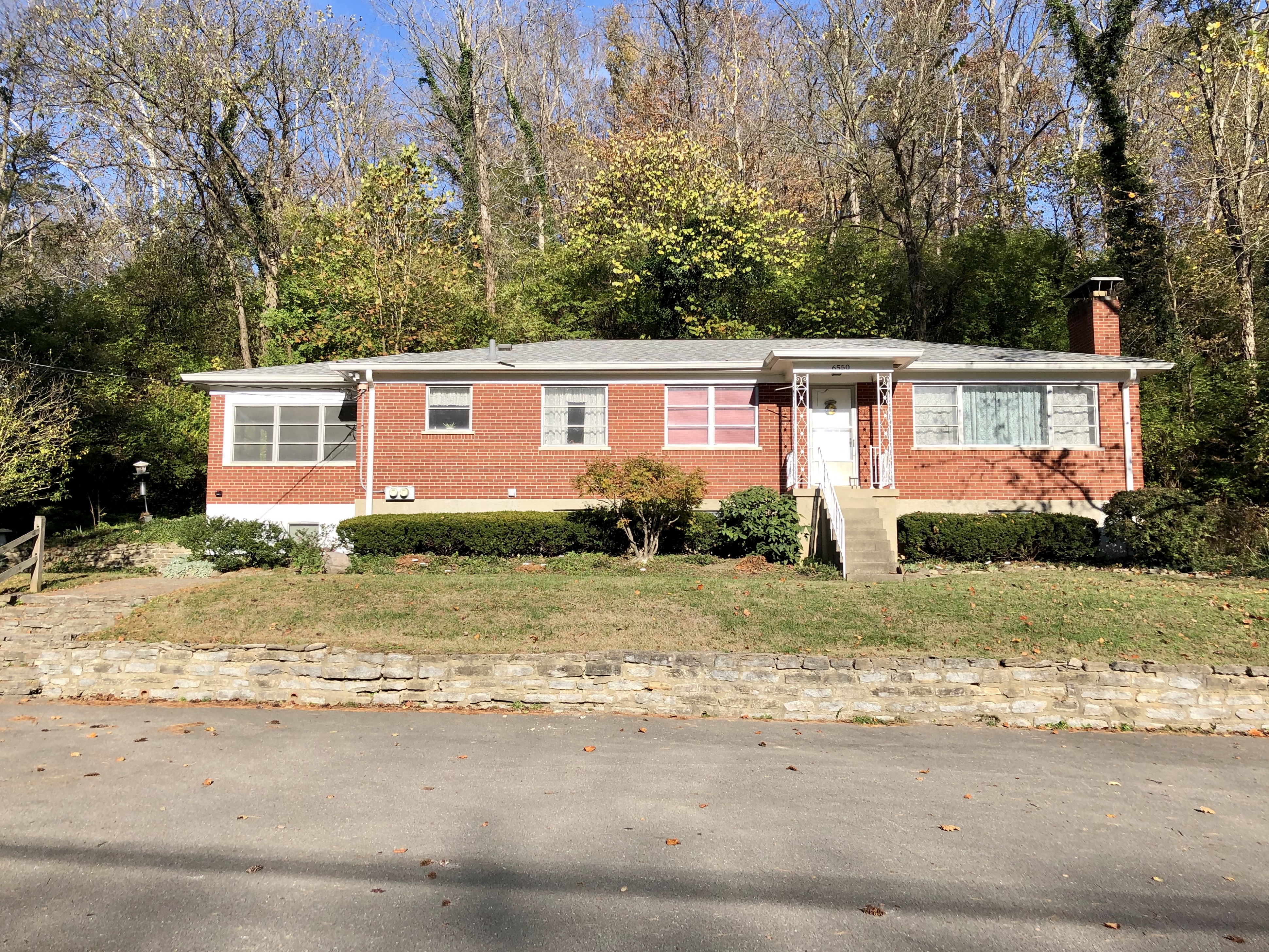 Single-story red brick ranch house on a raised lot with autumn trees behind it.
