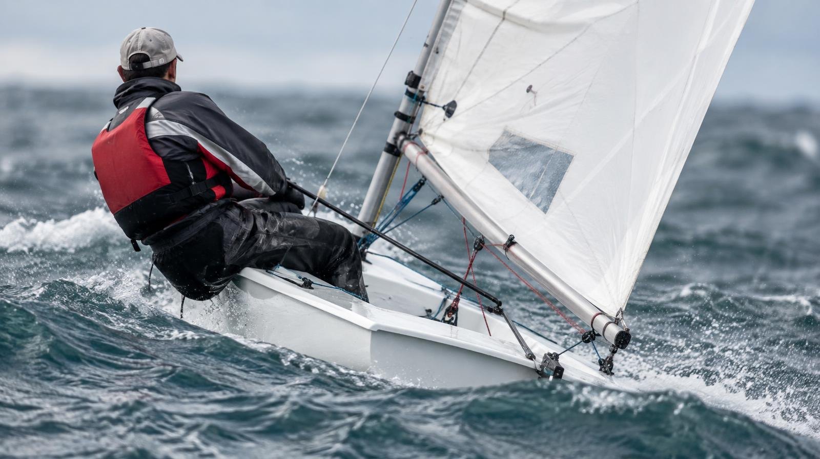 A small sailing dinghy heeling on choppy open water with sail trimmed.