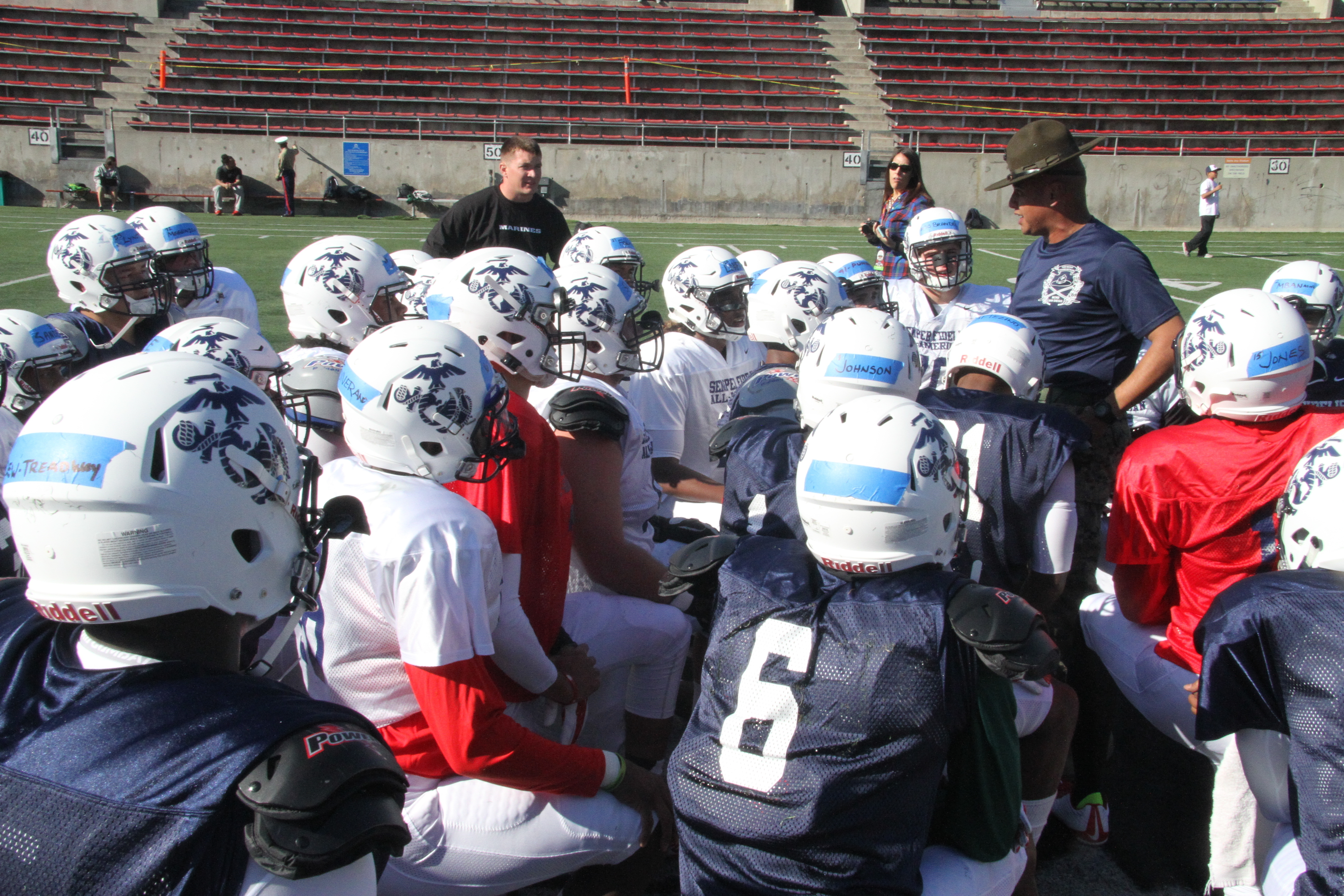 Football players in white and navy helmets huddled around coaches on a stadium field.