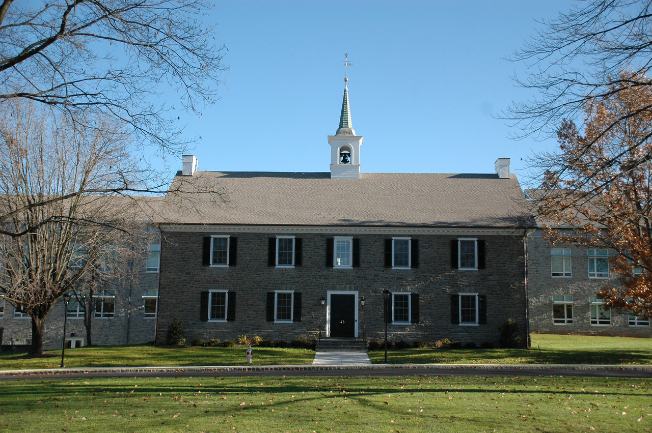 Stone colonial-style school building with white steeple and black shutters on a green lawn.