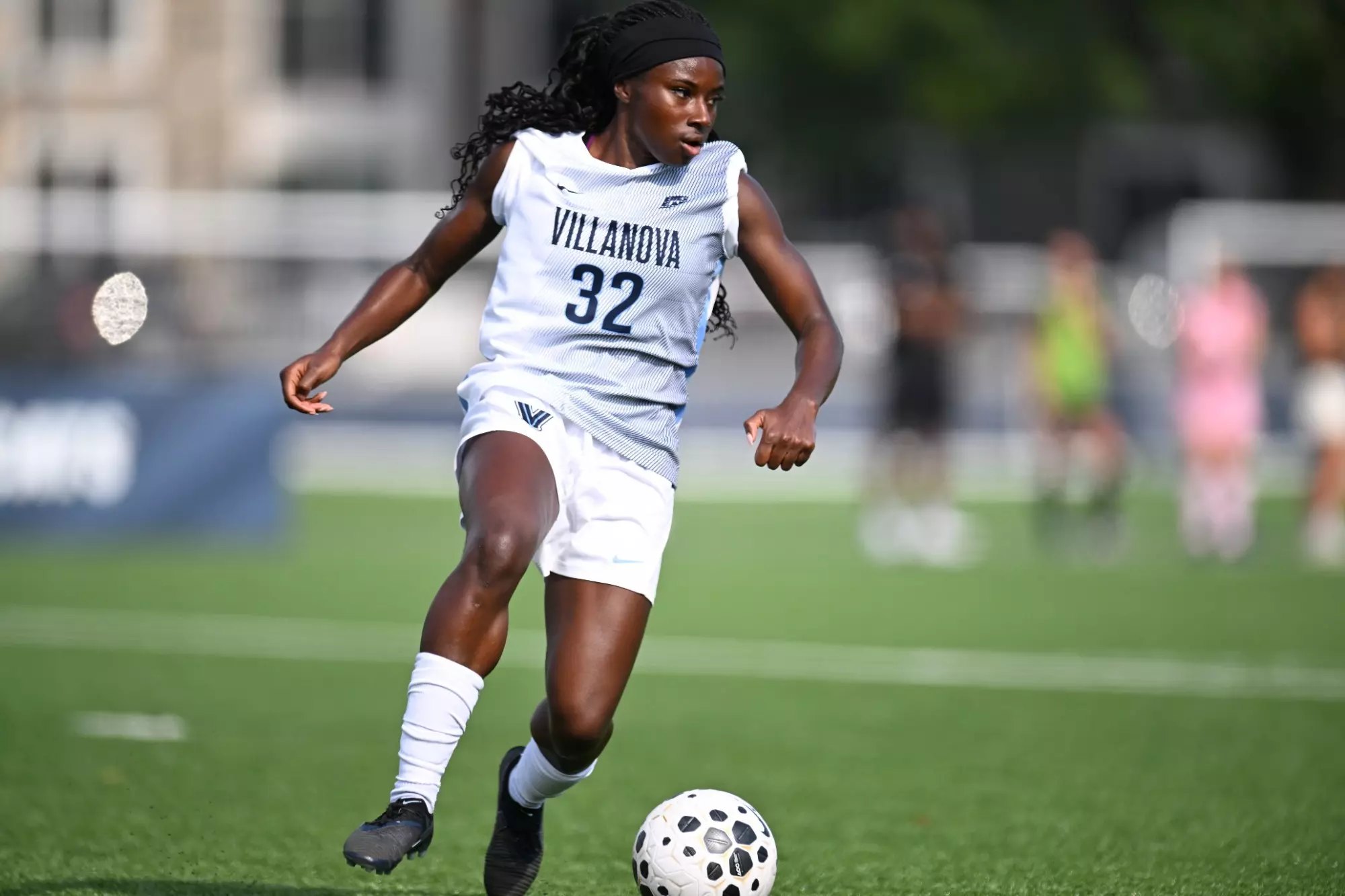 Female soccer player in white jersey numbered 32 dribbling a ball on a turf field.