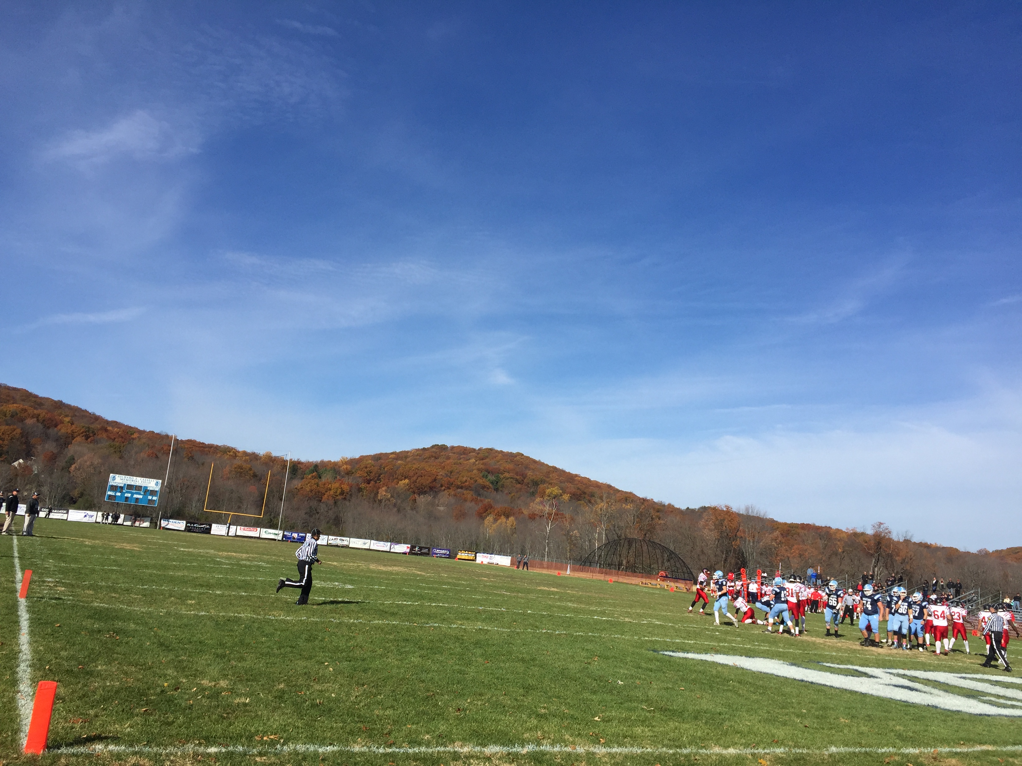 Football players in red and light blue uniforms compete on a grass field in New Jersey.