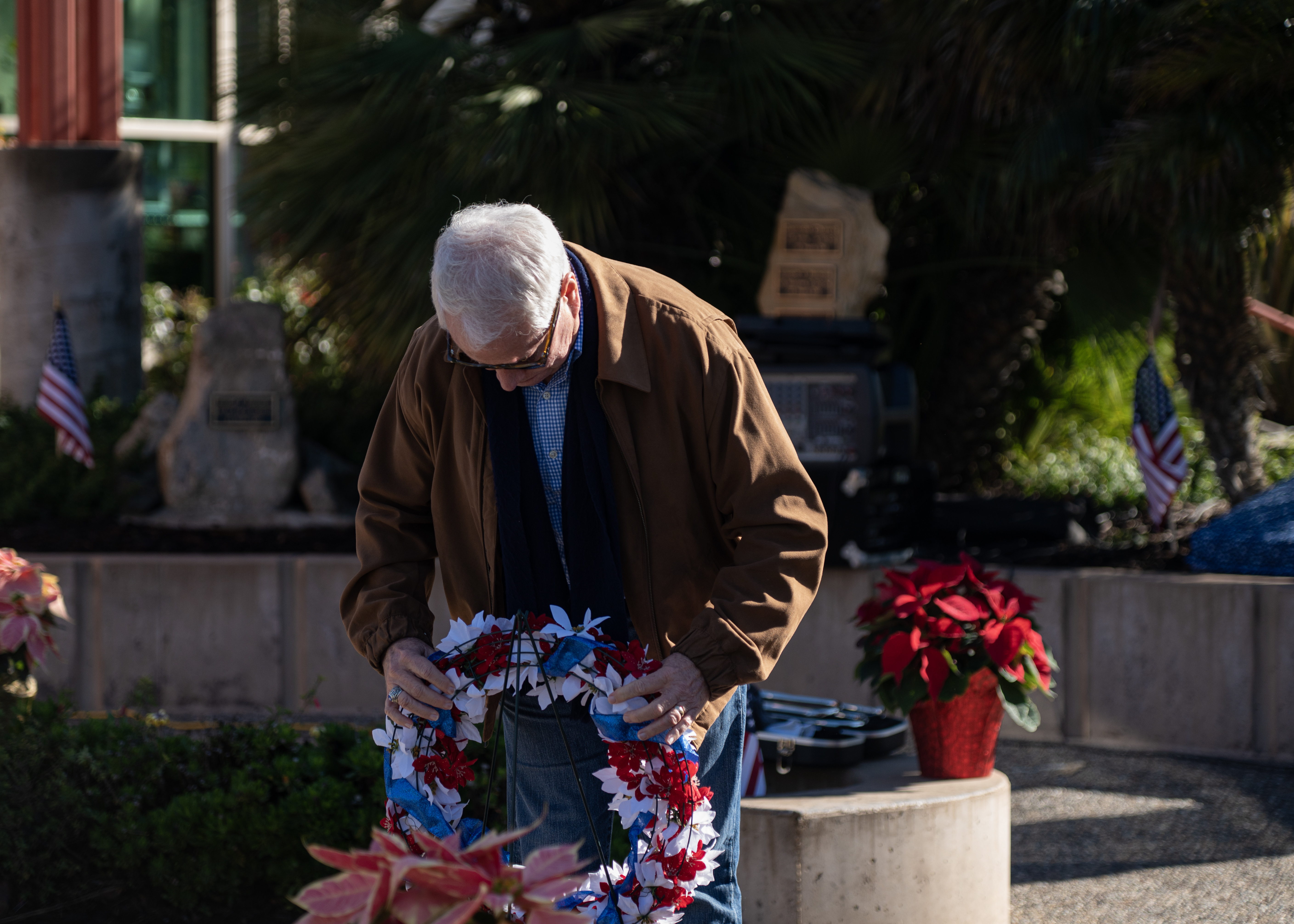 A person bends to place a red, white, and blue wreath at an outdoor veterans memorial.
