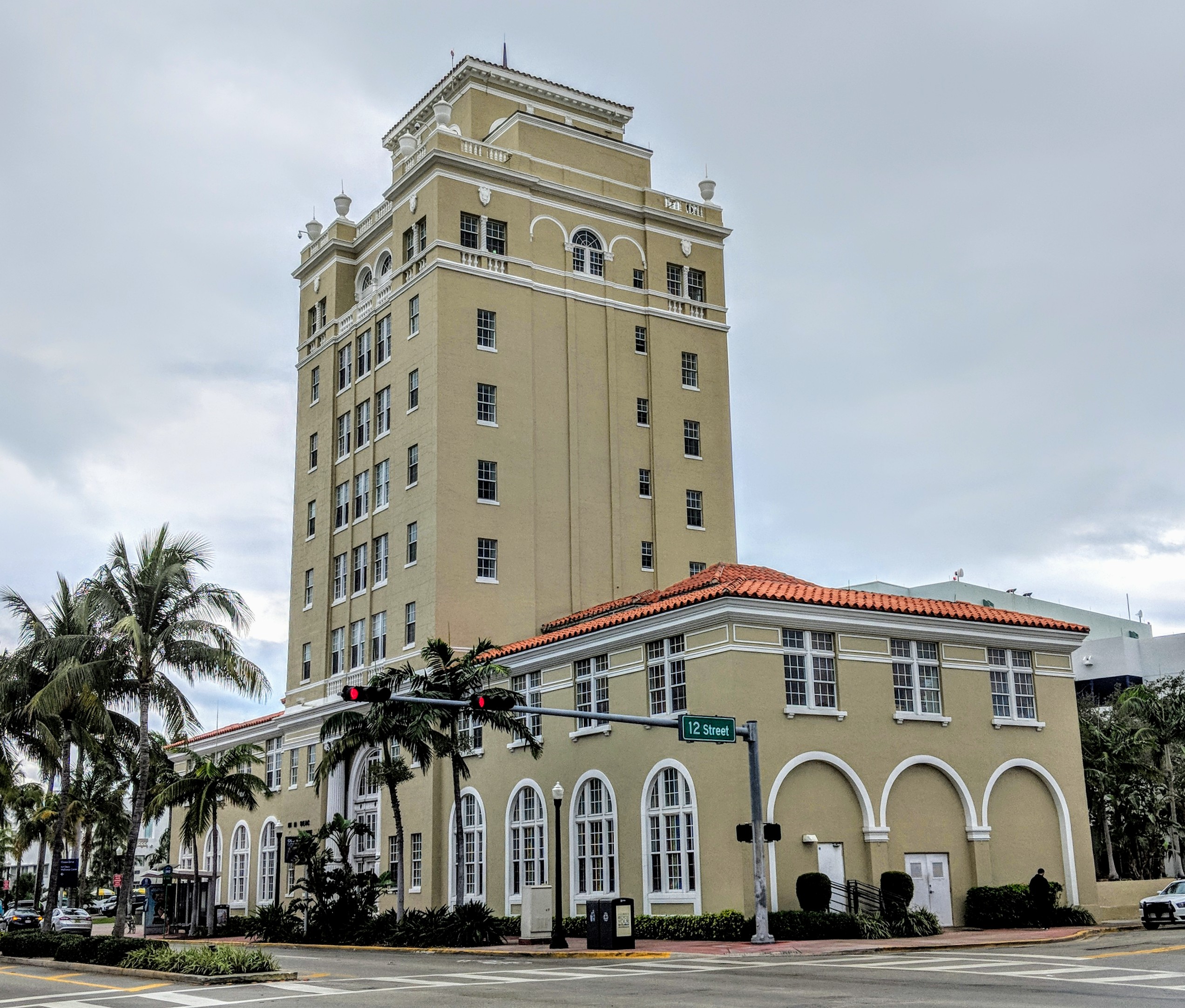 Multi-story Mediterranean Revival building at a Miami Beach street corner with palm trees.