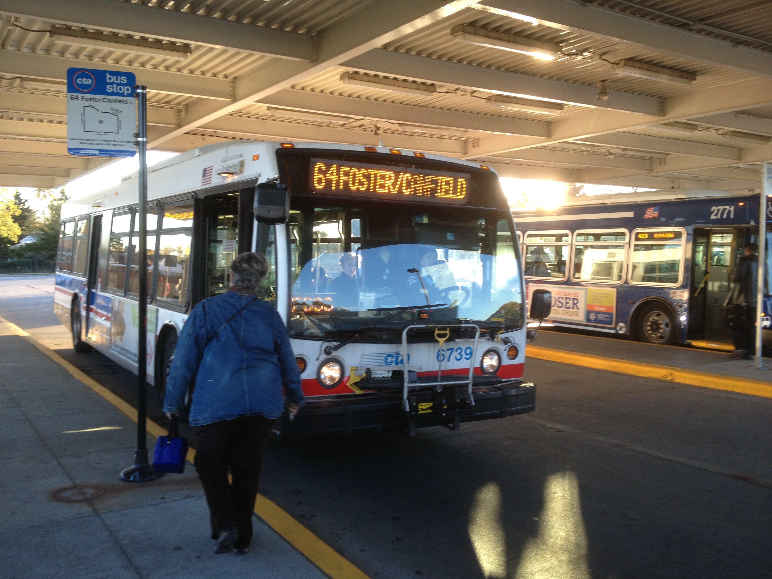 CTA bus stopped at an elevated Blue Line station with a pedestrian approaching.