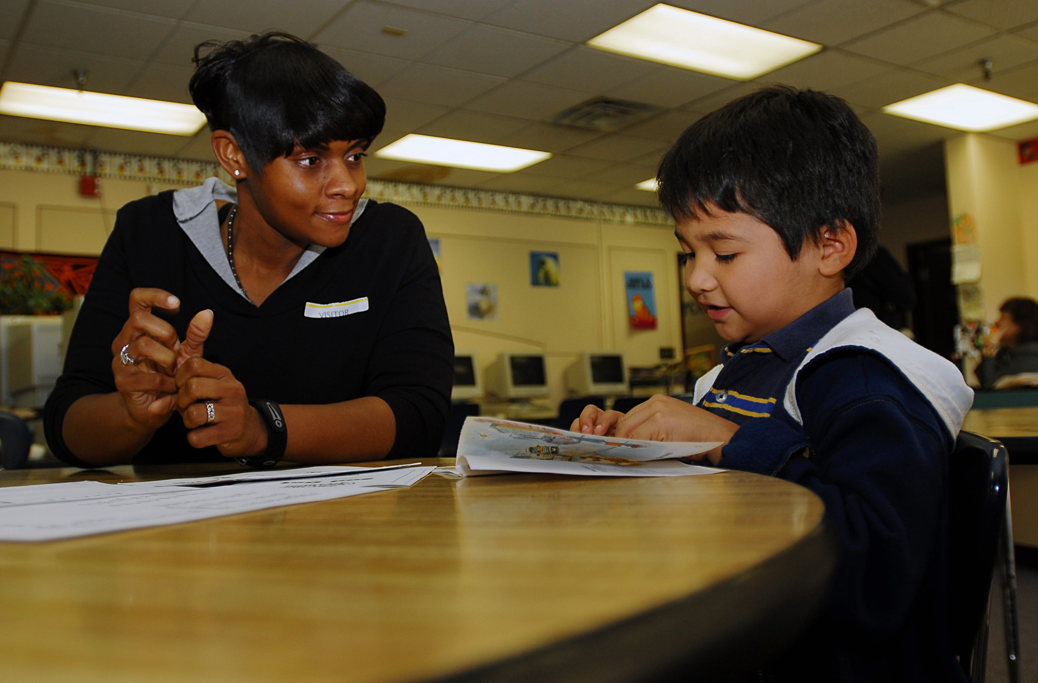 An adult woman and a young boy sit together at a round table reviewing a printed page.