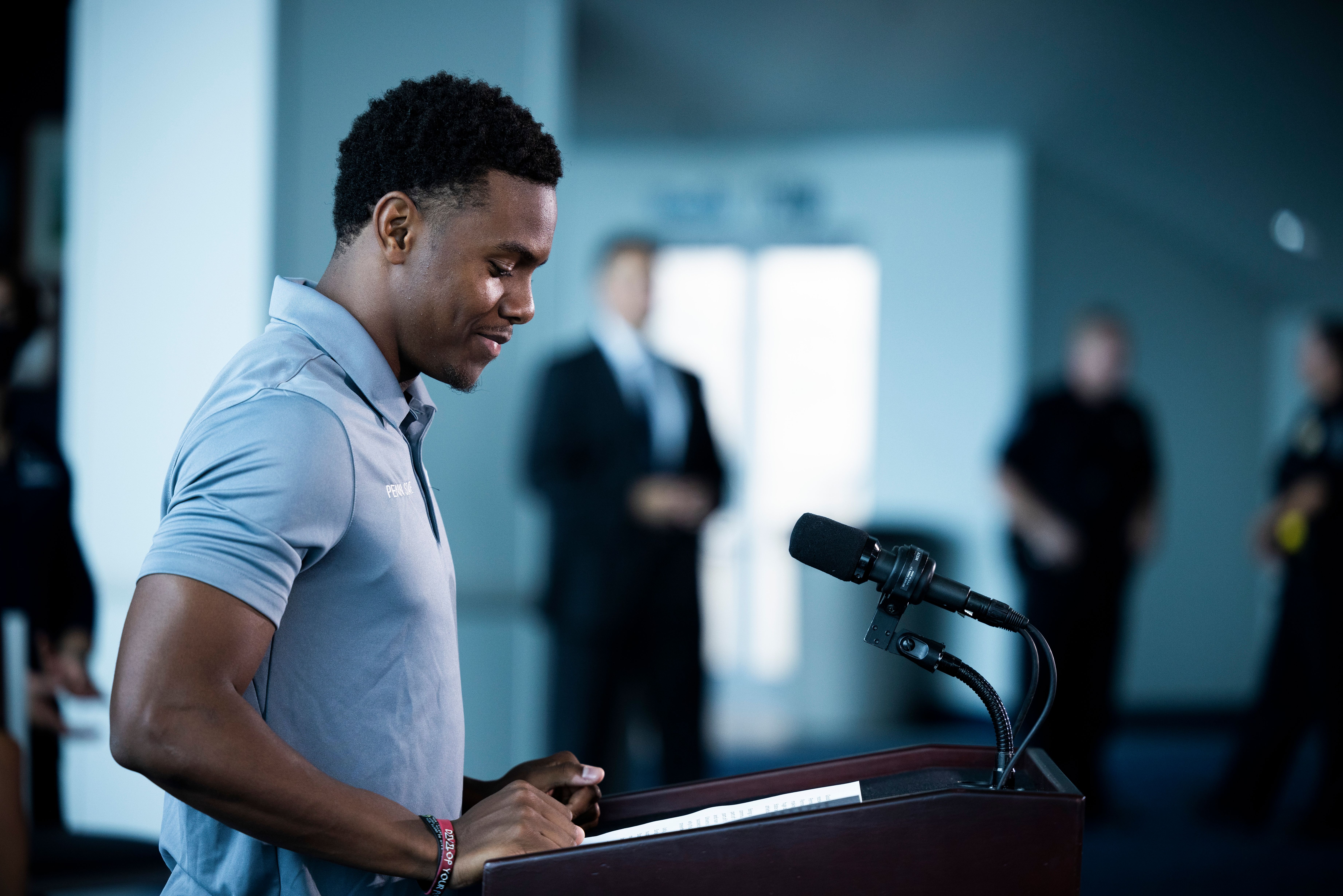 Young man in a gray polo shirt speaking at a podium with a microphone.