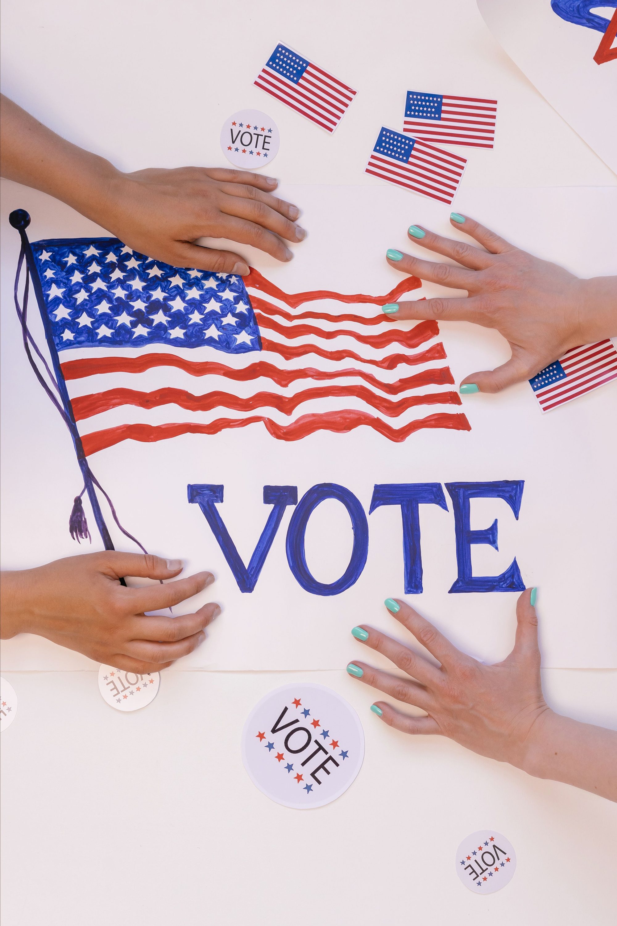 Hands arranging a patriotic voting poster with American flags, encouraging civic participation.