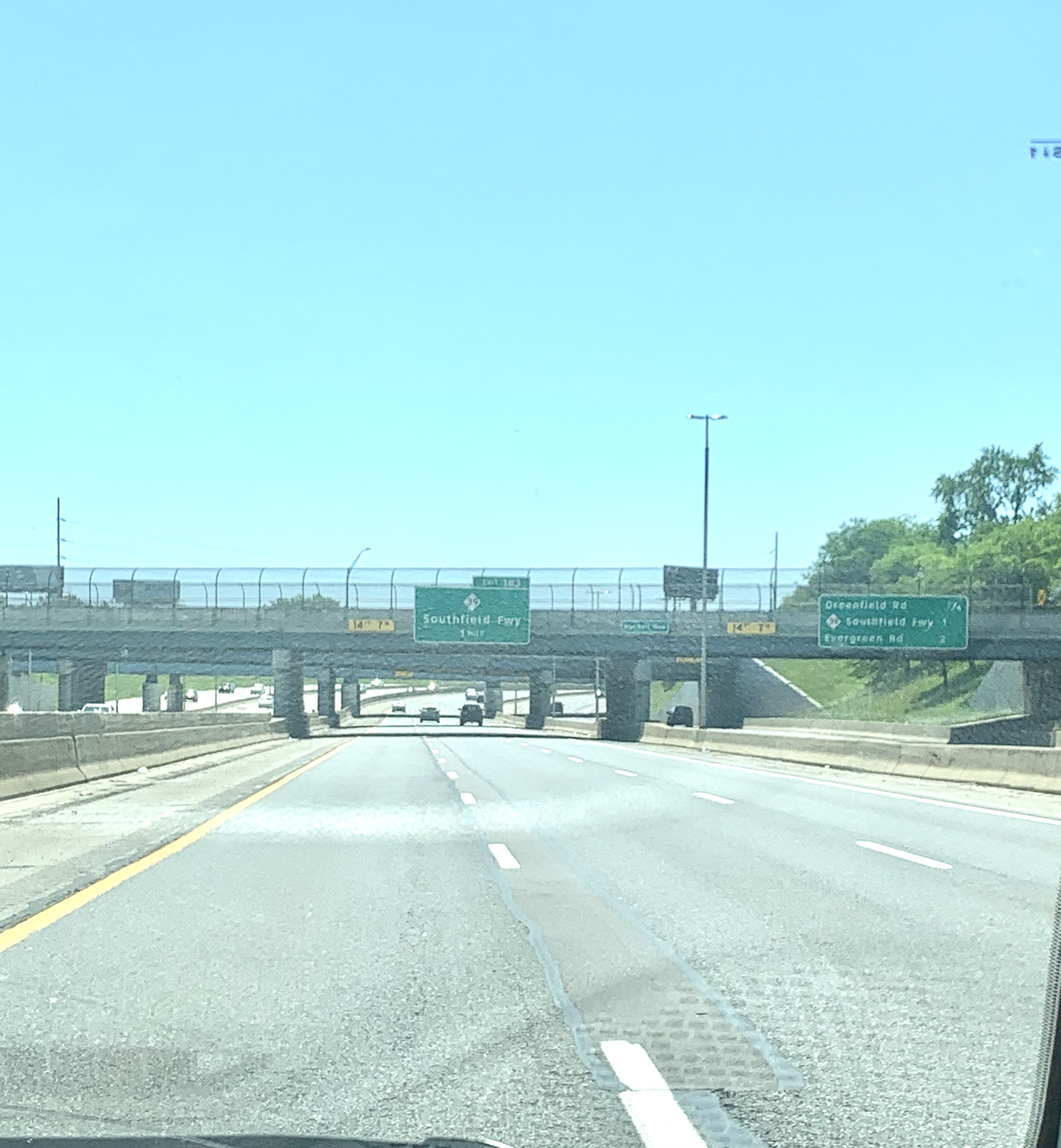 Multi-lane freeway with overhead green signs marking the Southfield Freeway exit under a blue sky.