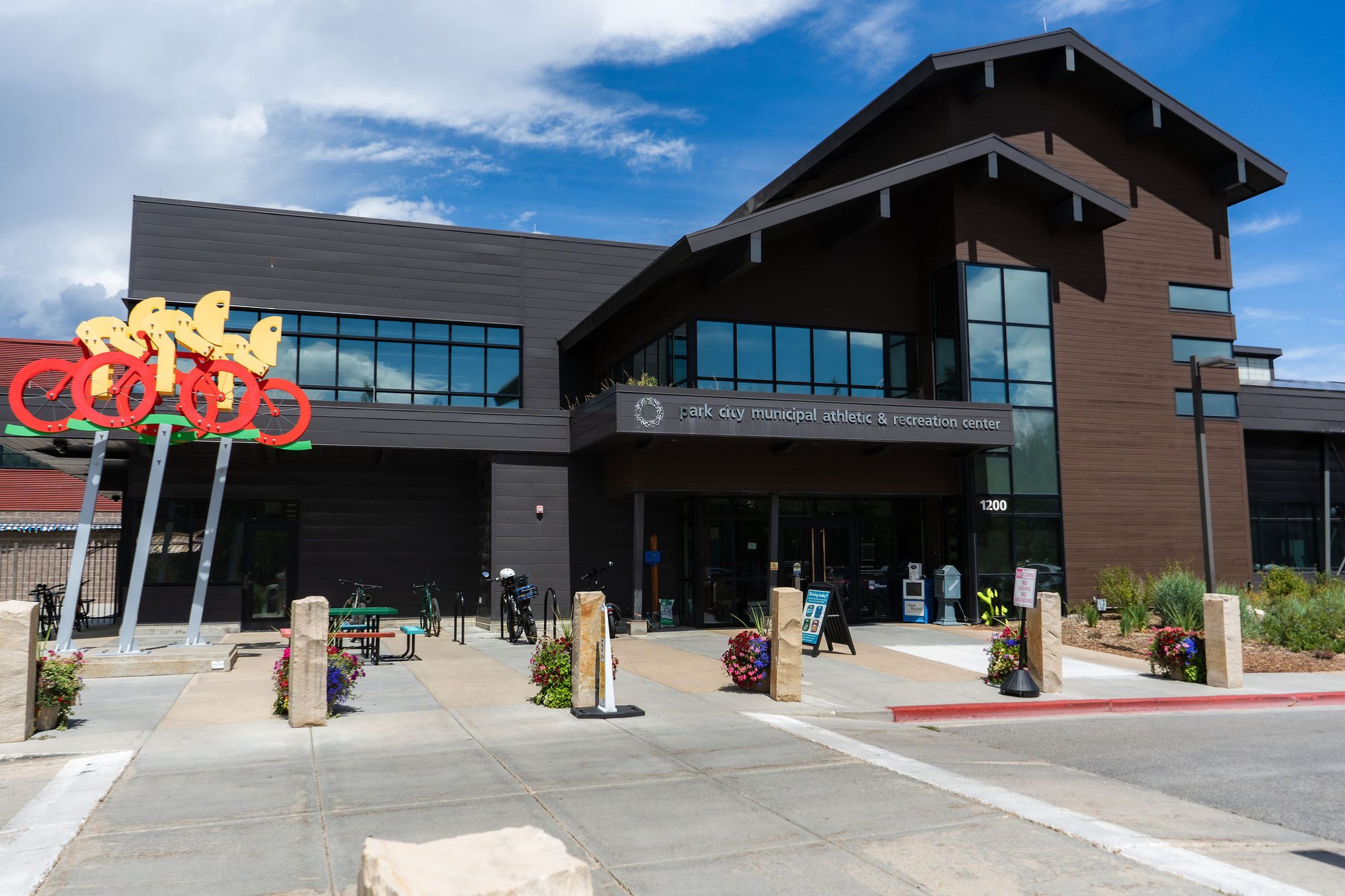 Exterior of a modern recreation center with large windows and a colorful sculpture near the entrance.
