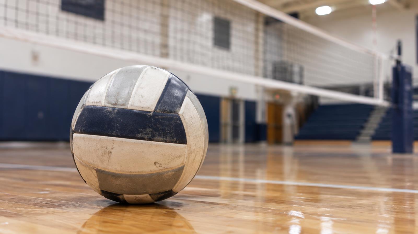 A volleyball resting on a hardwood gym floor near the net with court markings visible.