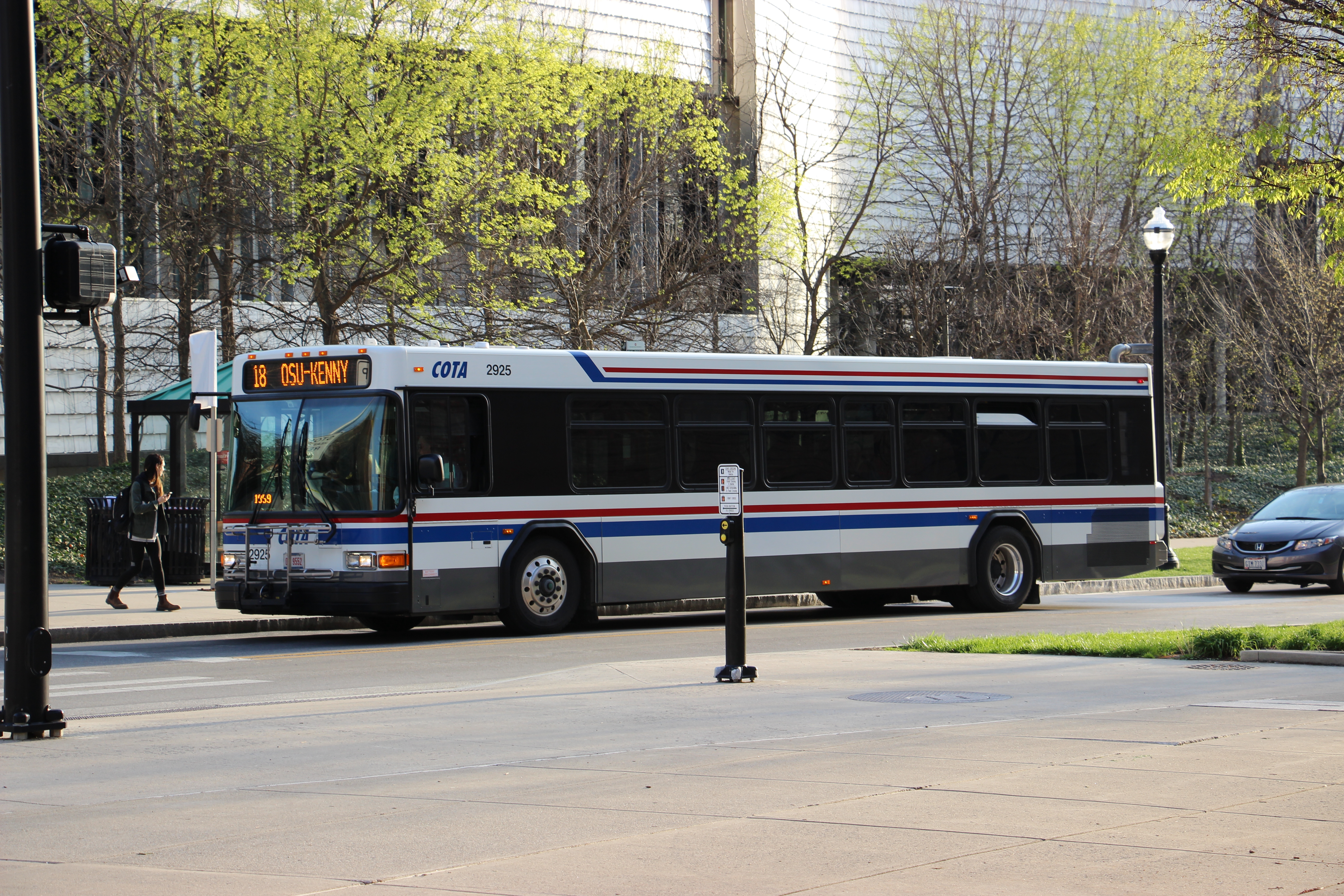 A COTA bus stopped on a tree-lined street near a university campus.