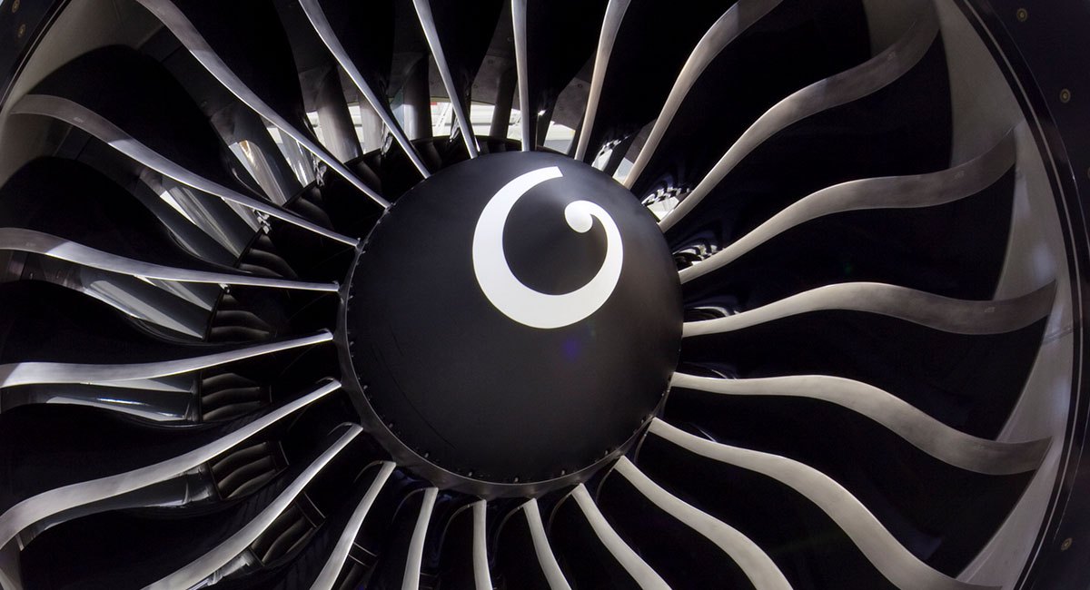 Front view of a large turbofan jet engine showing swept composite fan blades and a black spinner cone.