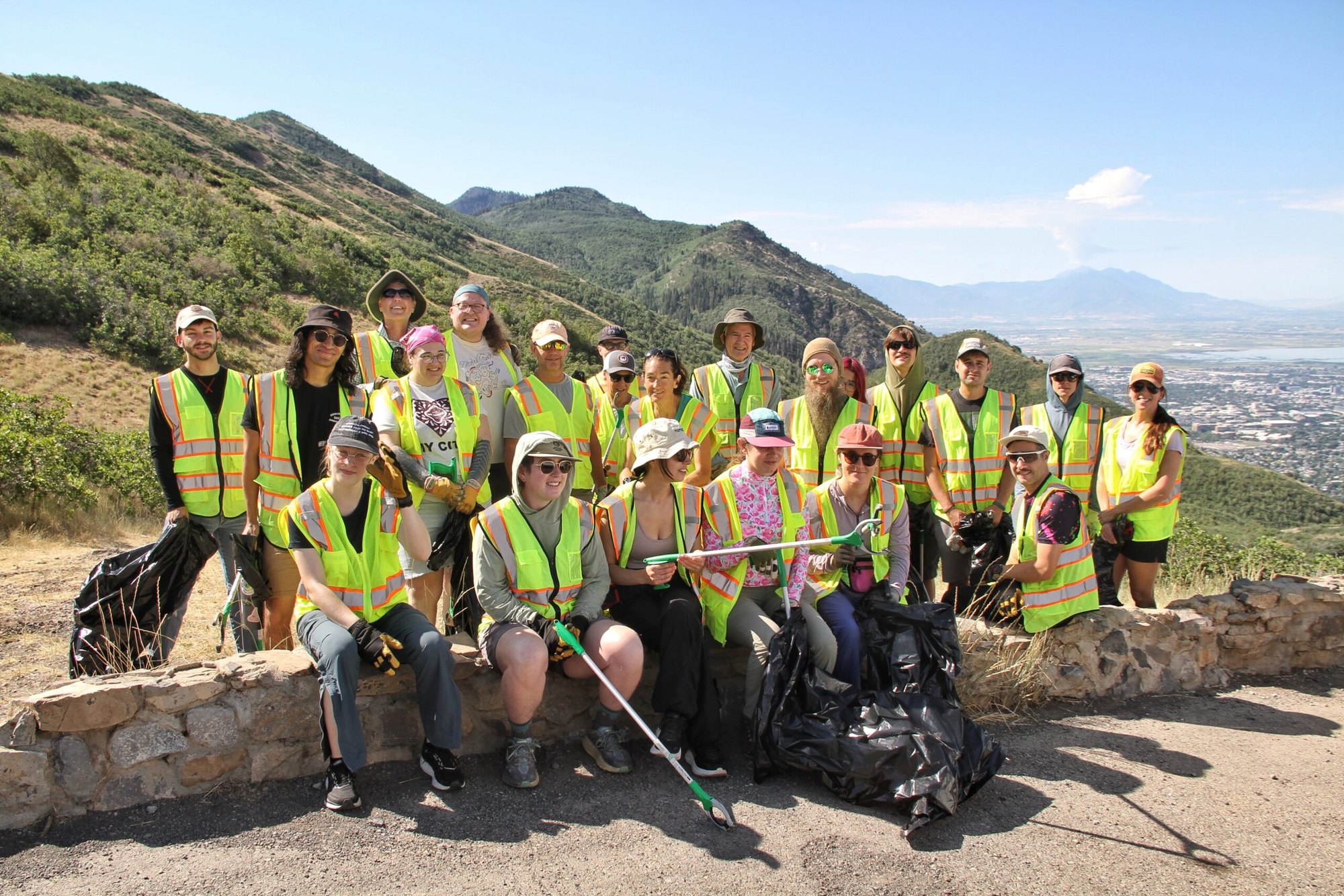 About twenty volunteers in neon vests hold trash bags and litter pickers at a canyon overlook.