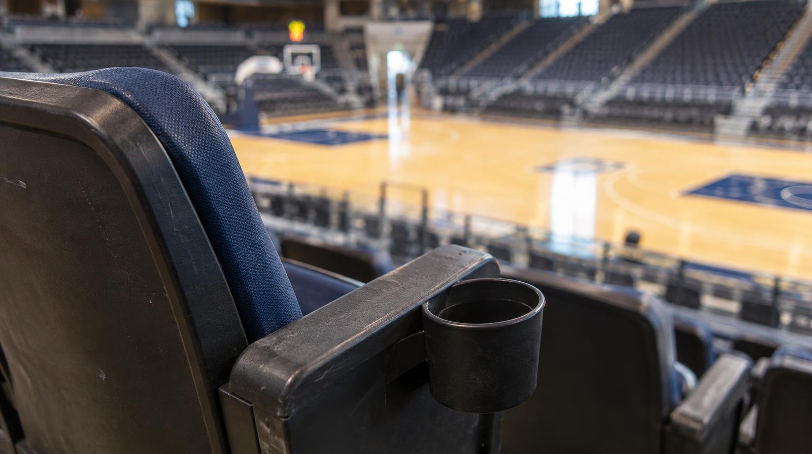A single folded arena seat with armrest and cup holder above an empty basketball court.
