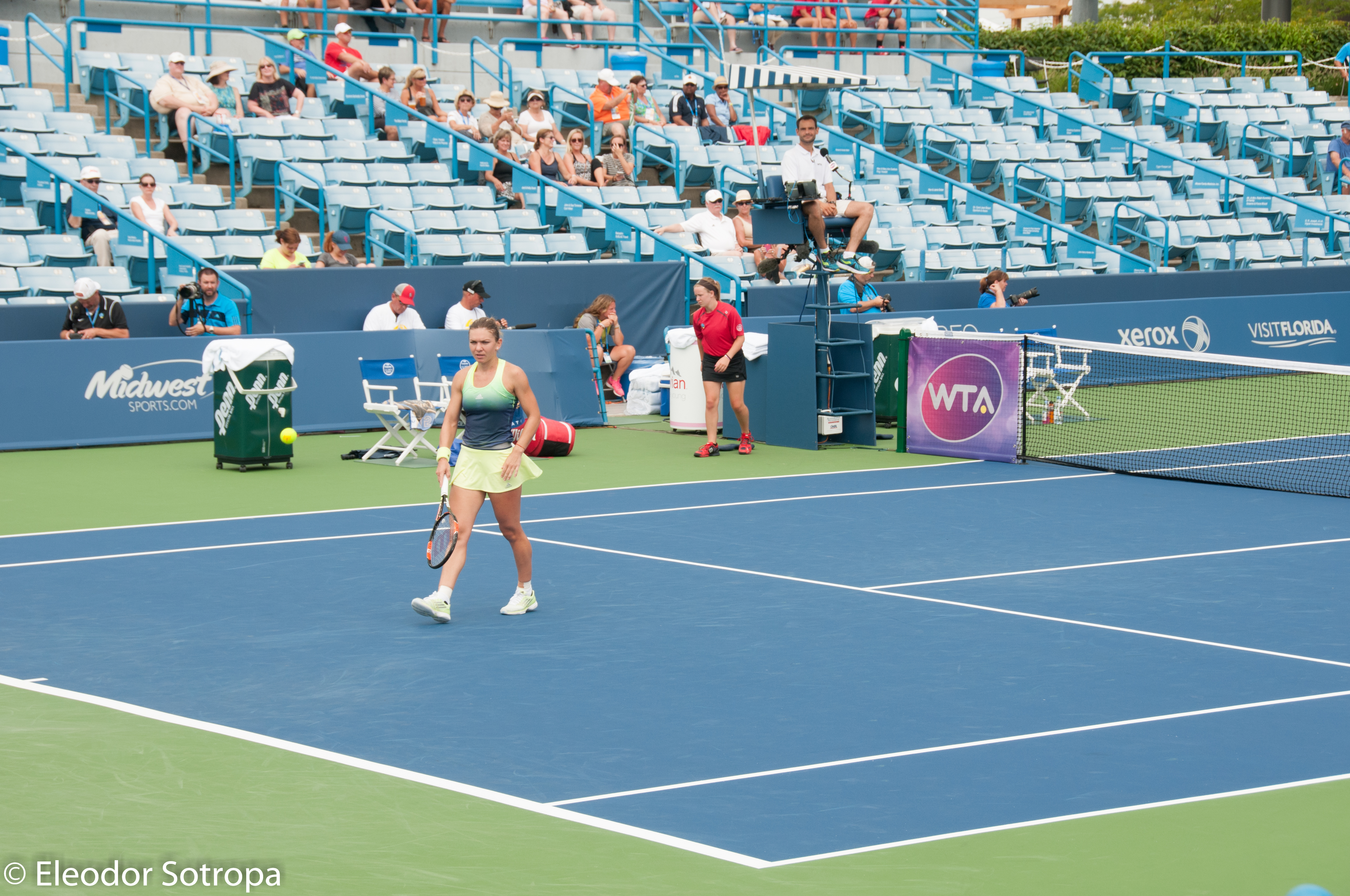 Female tennis player mid-match on a blue hard court with spectators in the stands.