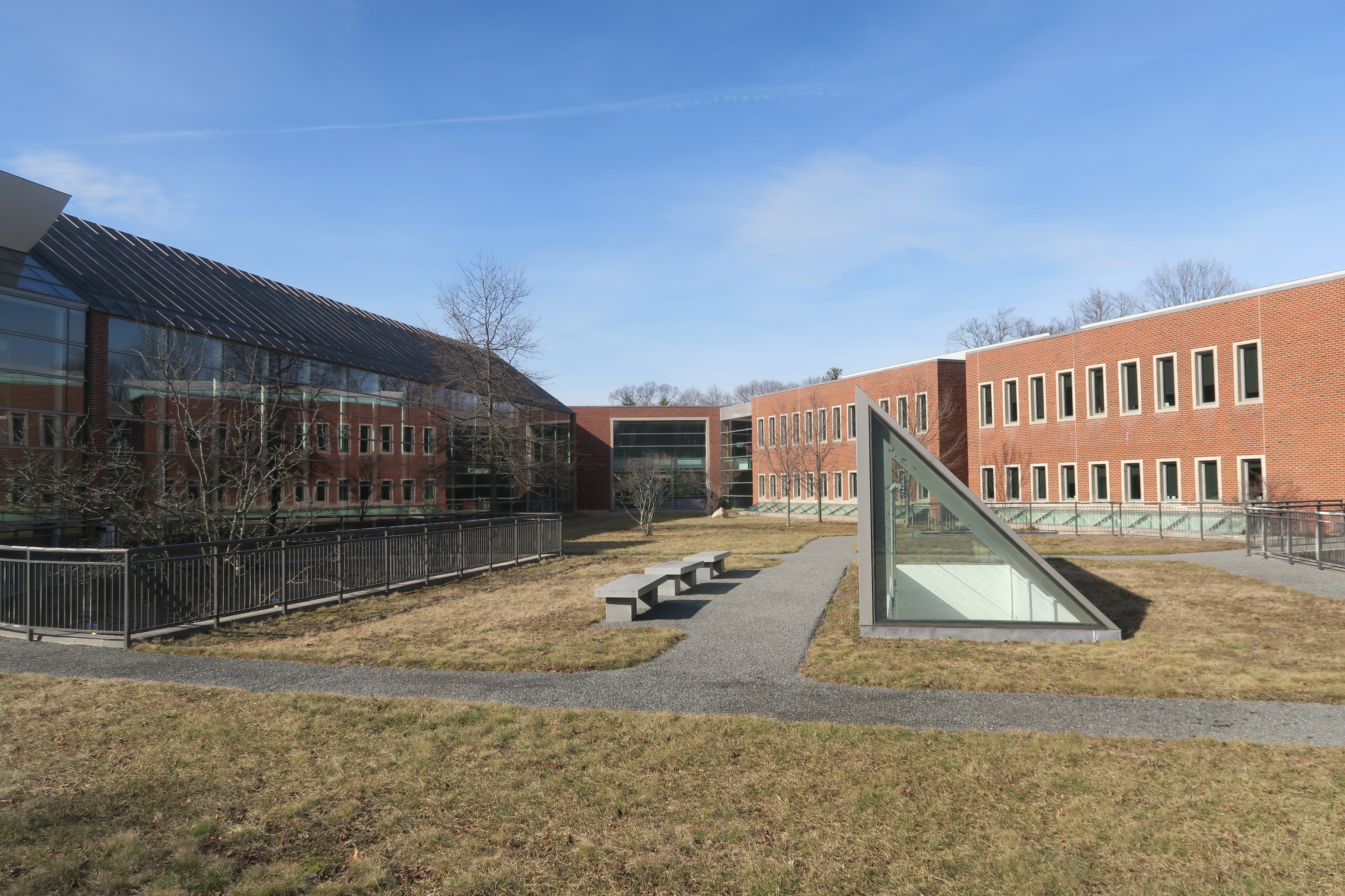 Red-brick college campus courtyard with a triangular glass skylight structure and bare trees.