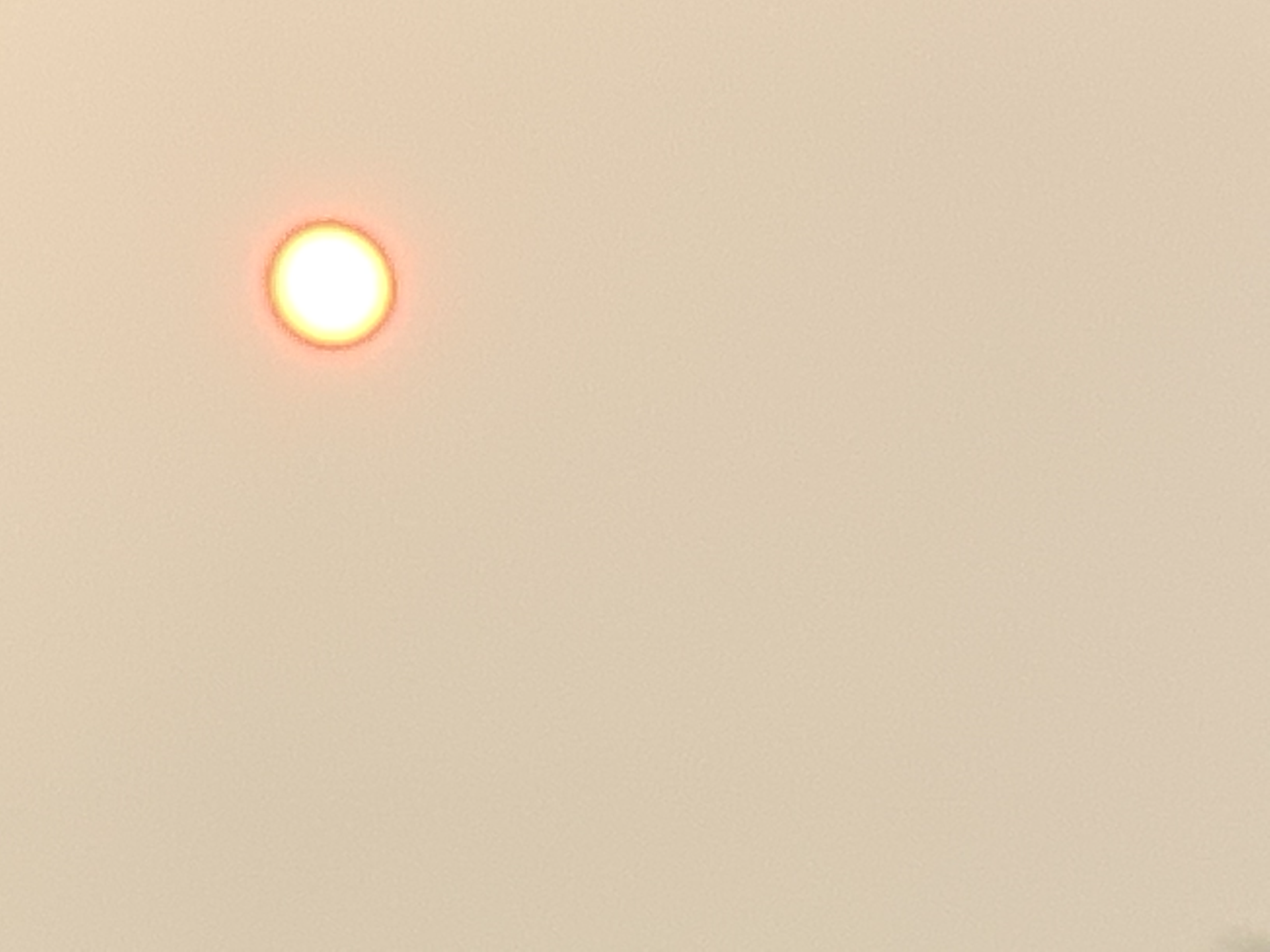 The sun visible as a pale orange disc against a uniformly hazy, smoke-filled sky.