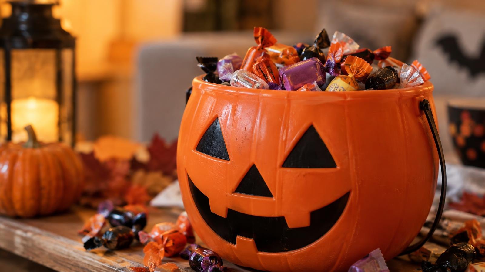 An orange jack-o-lantern bucket overflowing with colorful wrapped Halloween candy.