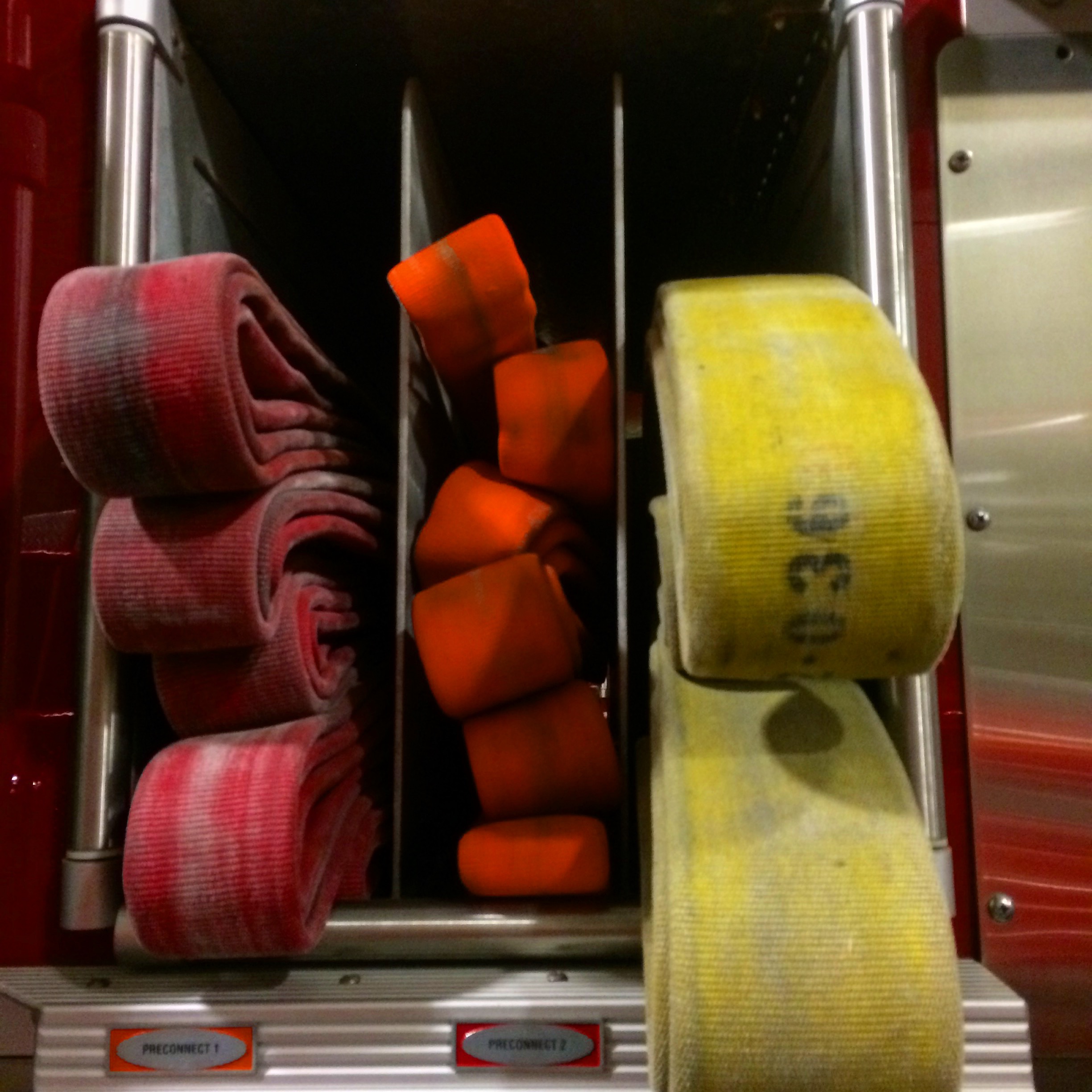 Three compartments of a red fire truck holding rolled fire hoses.