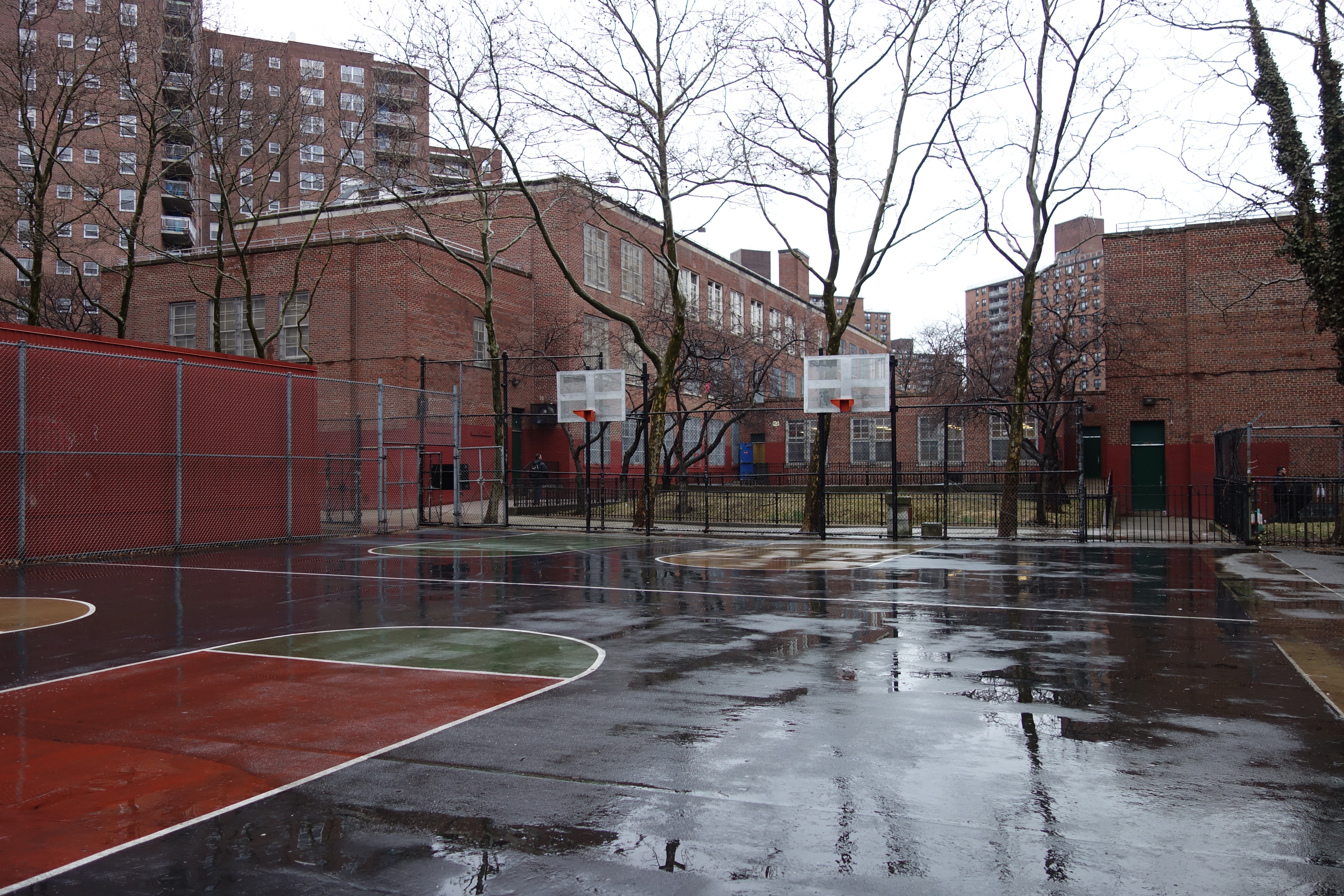 Wet outdoor basketball courts with colorful painted surfaces and chain-link fencing.