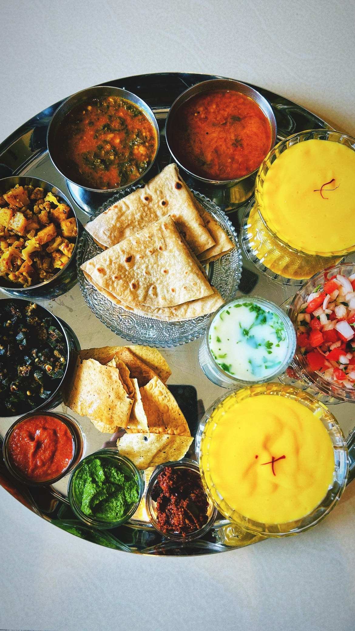 Silver thali platter with small bowls of curries, flatbread, chutneys, and a saffron-garnished dessert.