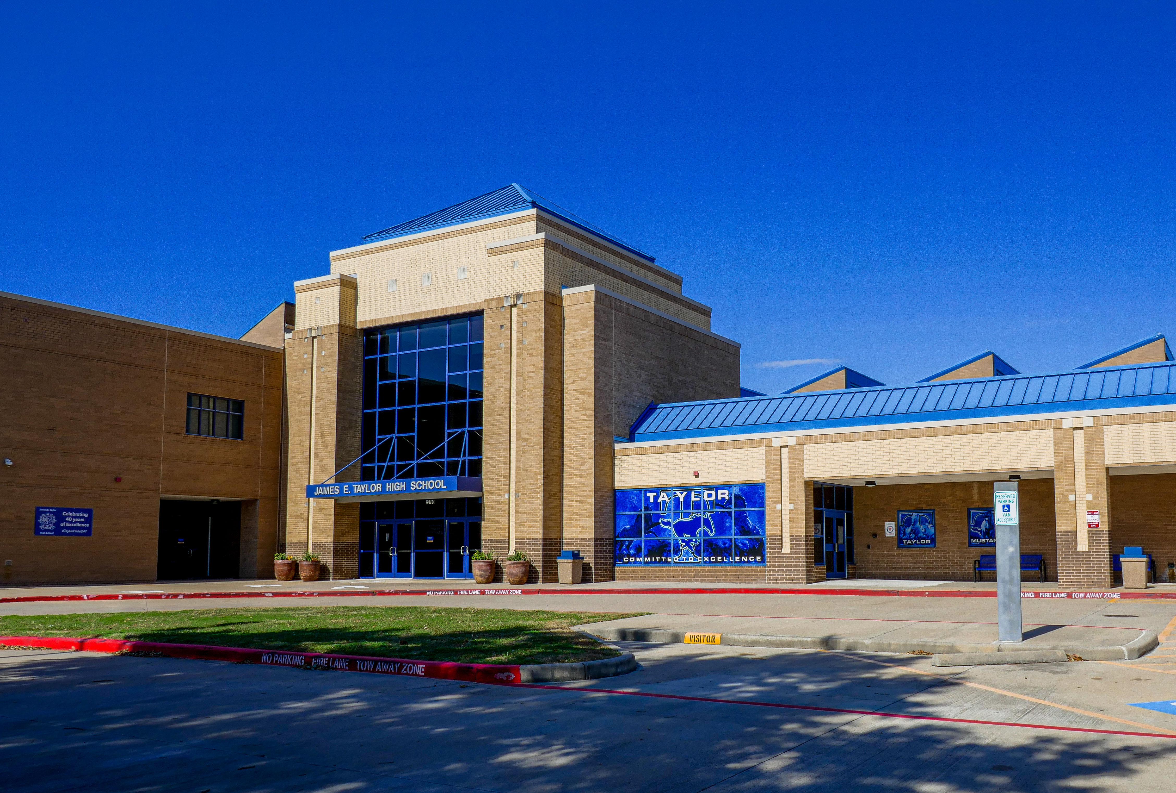 Brick high school building with blue roof accents and glass entrance displaying the name Taylor.