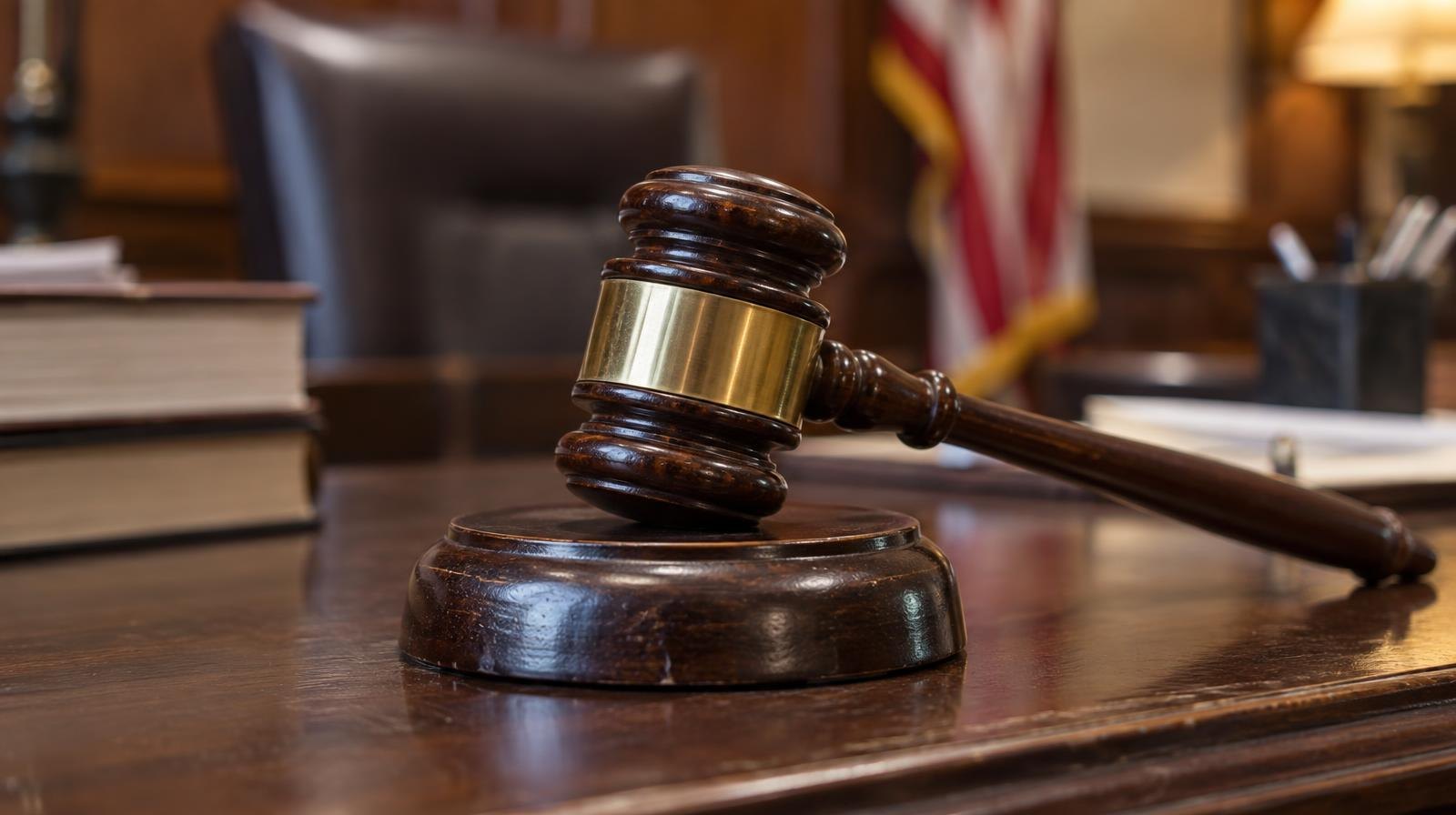 A wooden judge's gavel resting on its sound block on a dark wood surface.