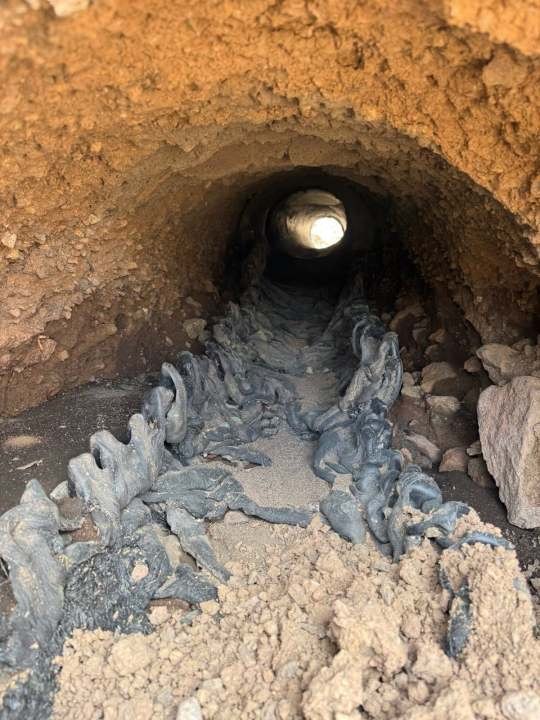 Inside a culvert tunnel with charred, melted debris on the floor and walls.