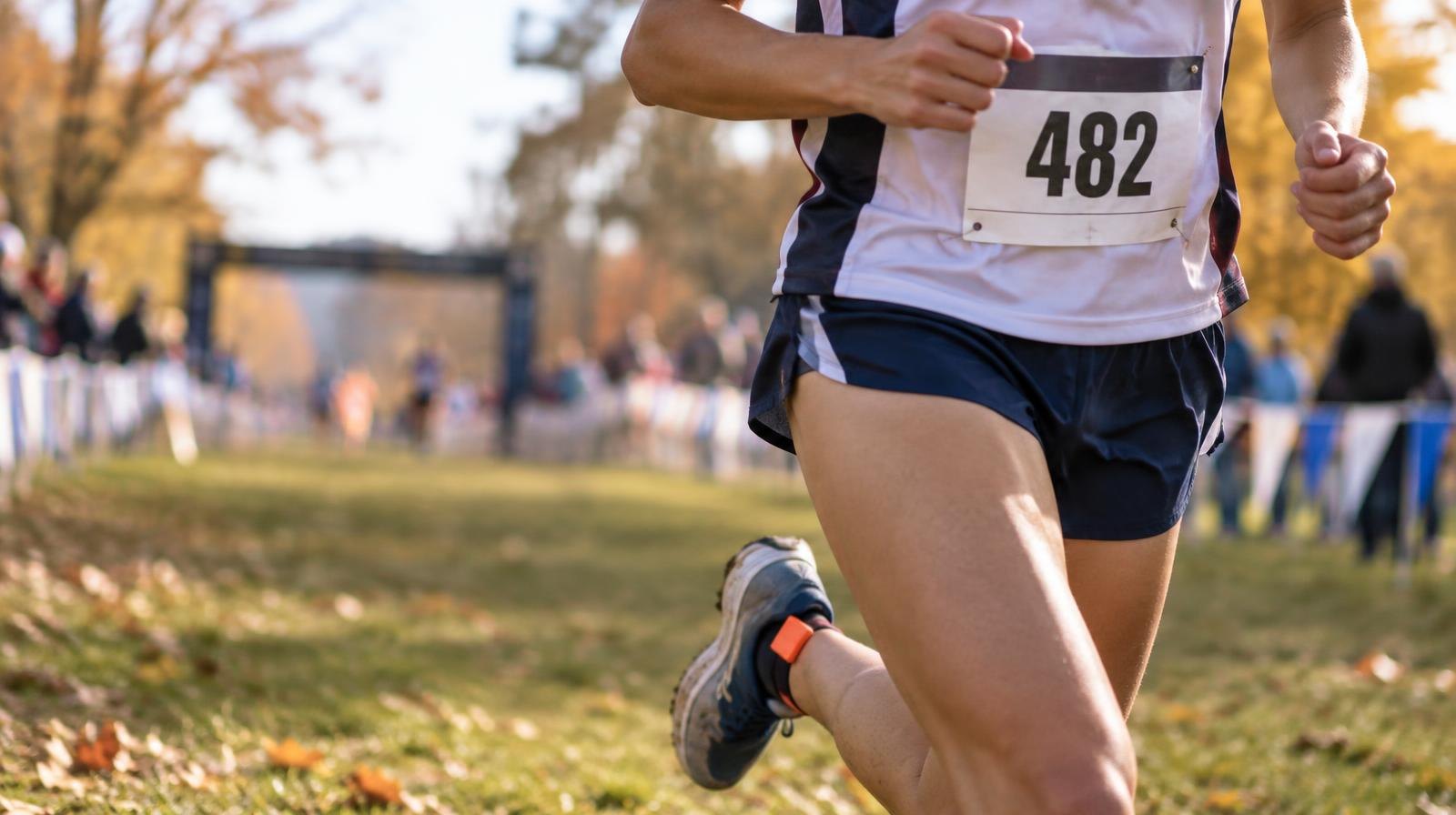 A racing bib pinned to a singlet beside running shoes on a grass course.