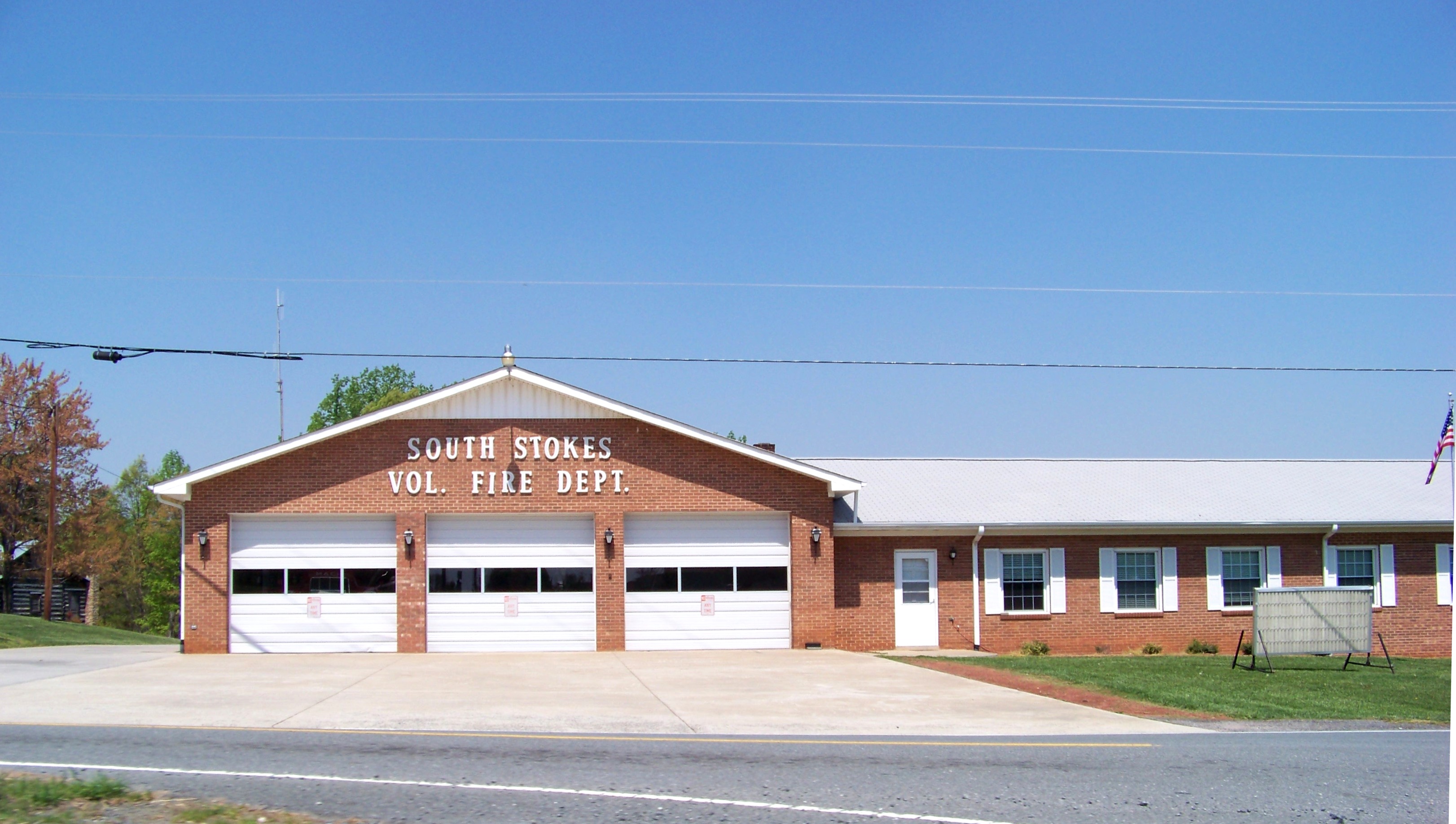 Brick volunteer fire station building with three white overhead bay doors.
