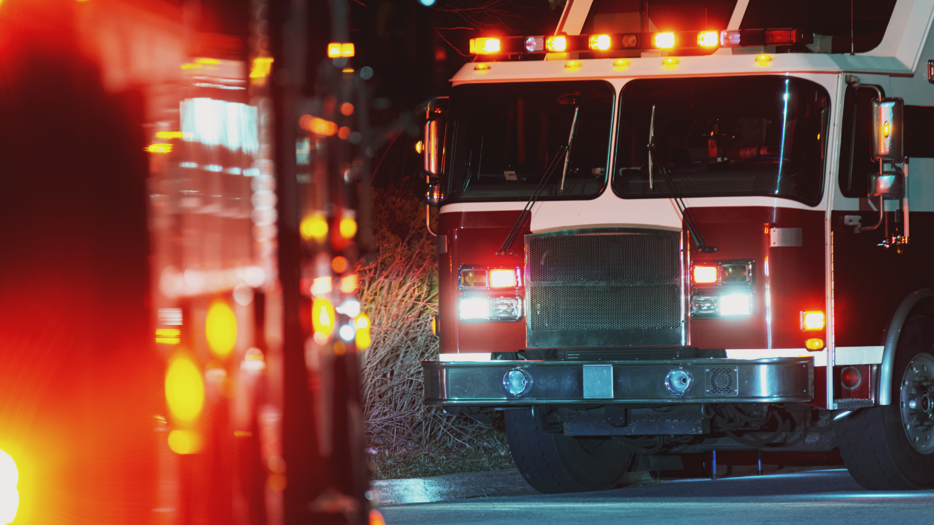 Two red fire trucks with emergency lights on at a scene.