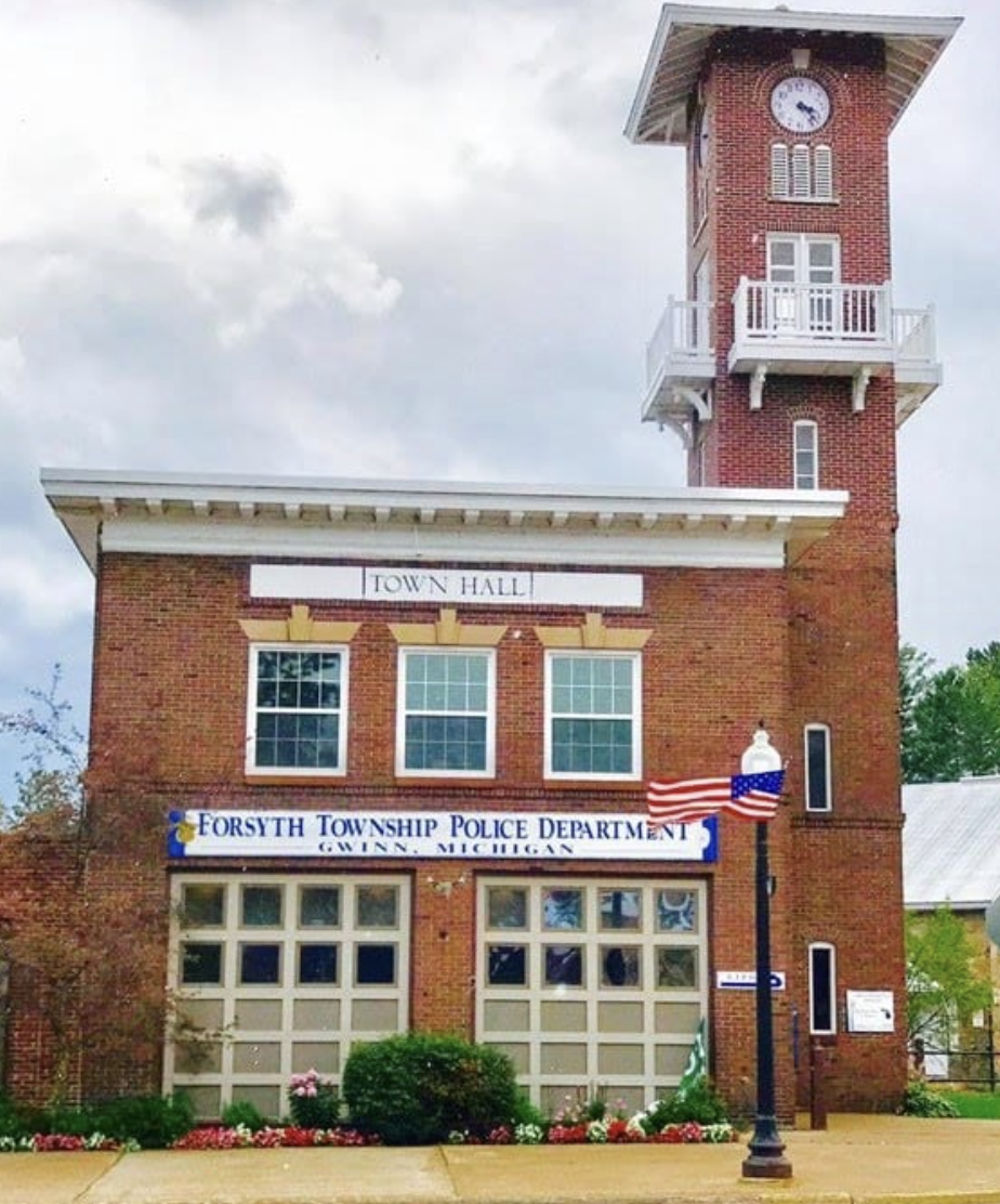 A brick town hall building with a tall clock tower houses the Forsyth Township Police Department in Gwinn, Michigan.